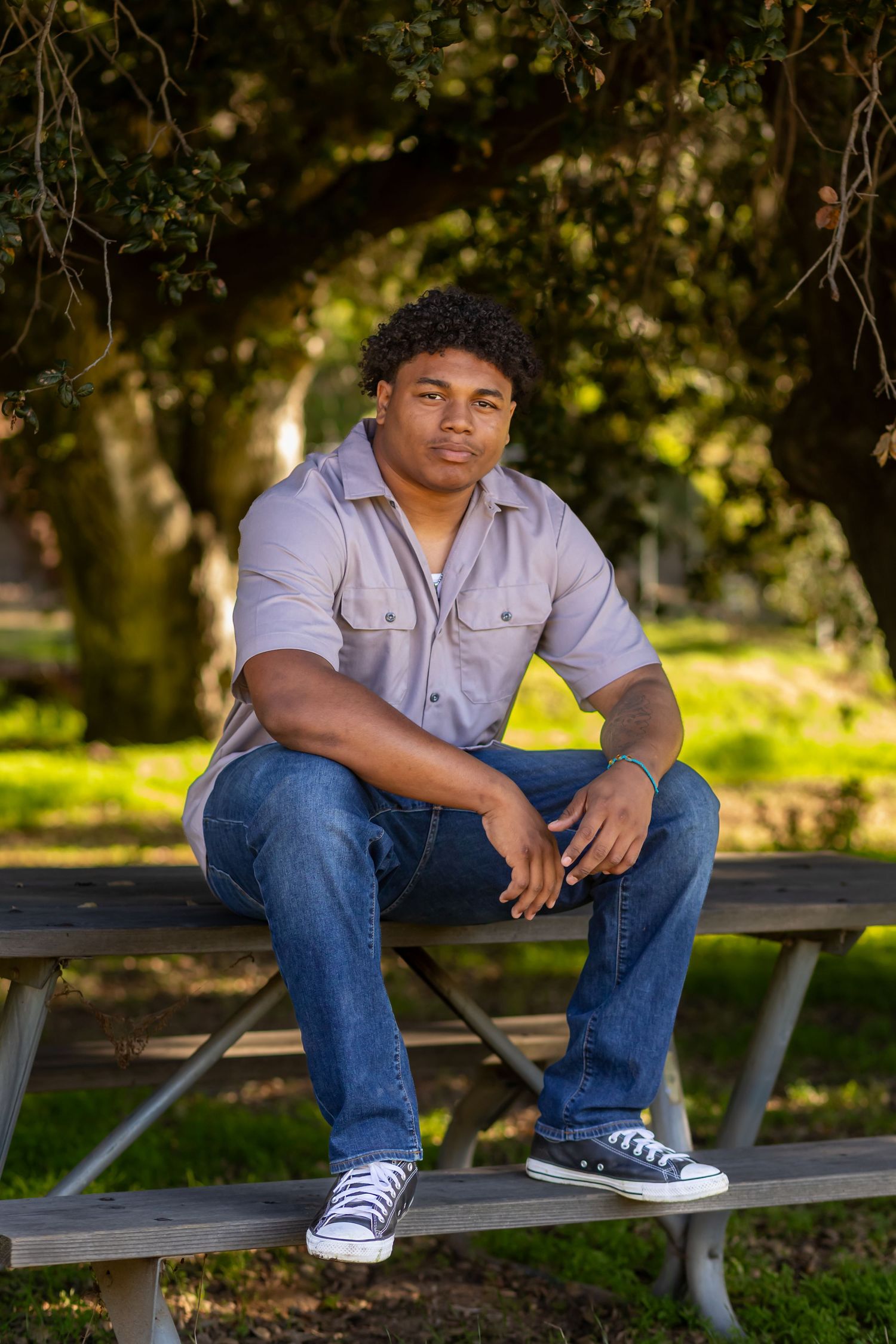 A casual portrait of someone seated on a picnic bench in a park setting with dappled sunlight in Yucaipa.