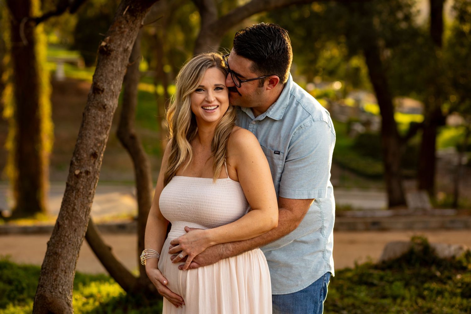A couple shares an intimate moment in a sun-dappled forest wearing casual clothing during an outdoor photo session.