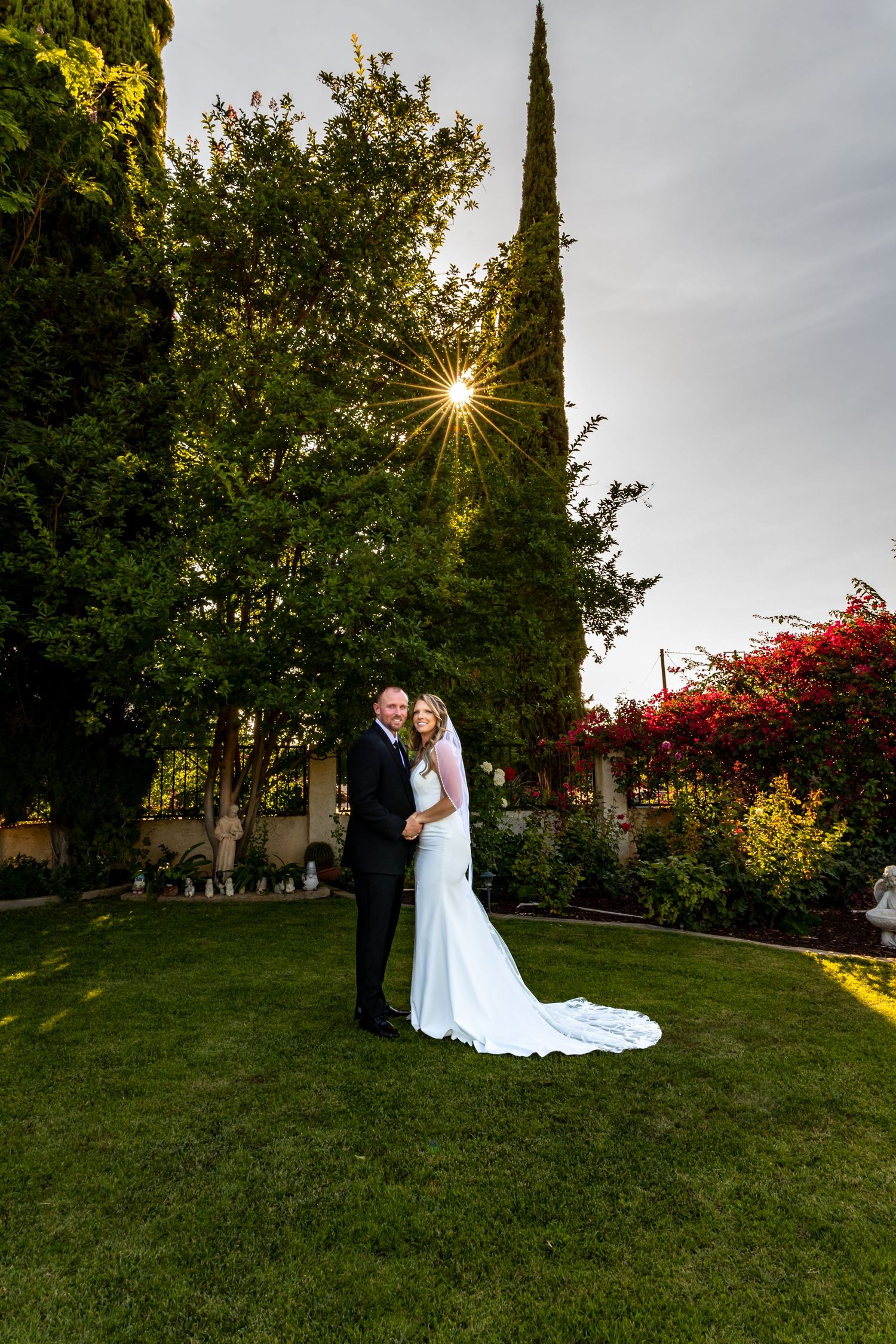 A scenic outdoor wedding photoshoot on a grassy hill with cypress trees and autumn foliage at sunset in Redlands.