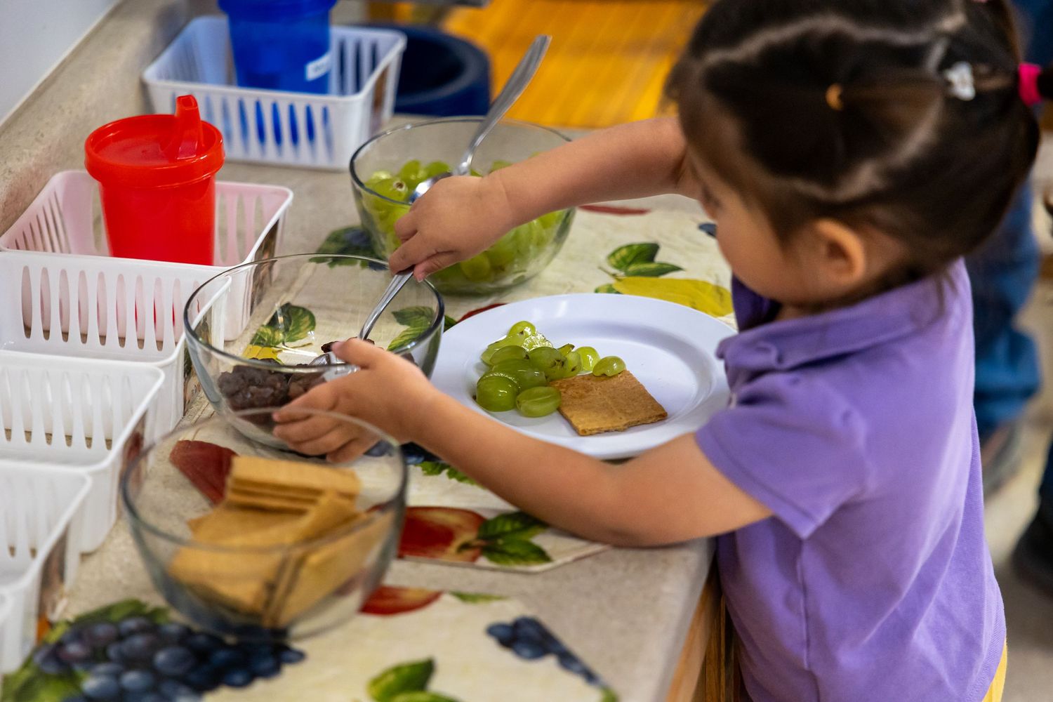 A child preparing food at a learning station with plates and ingredients laid out on a counter.