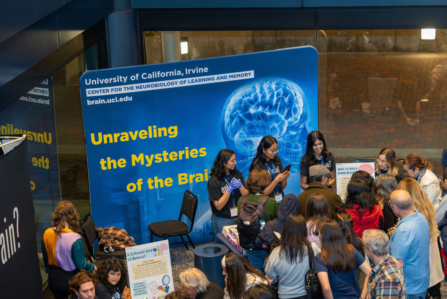 Students gather at a university research exhibition featuring brain science displays and informational banners.