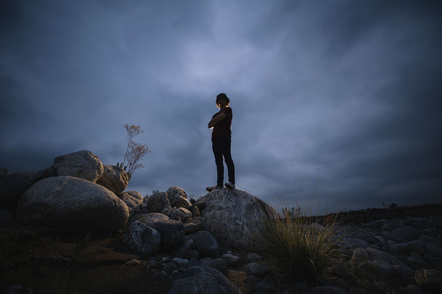 Silhouette of a Graduate standing on rocks against dramatic cloudy sky at dusk in Yucaipa.