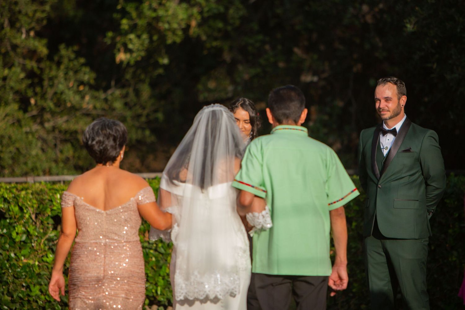 Wedding party walking outdoors with bride in white dress and attendants in formal attire.