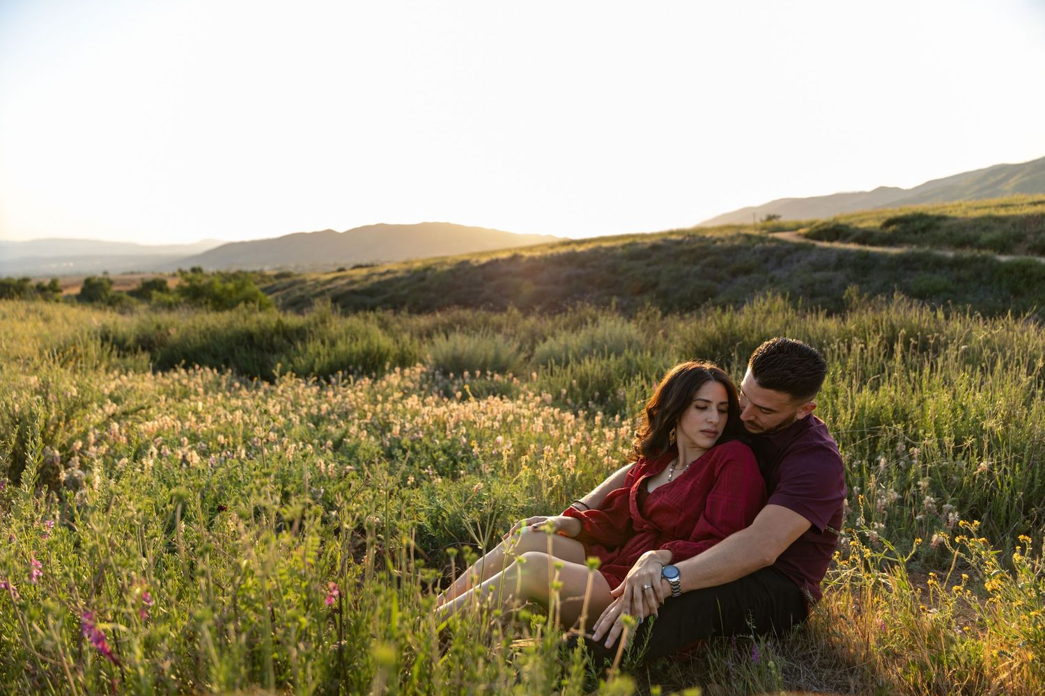 Couple sitting together in a meadow during golden hour with rolling hills in the distance.