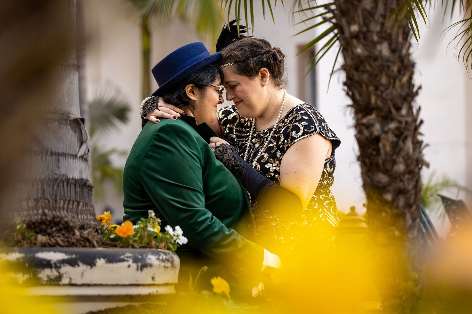 A couple shares an intimate moment outdoors with yellow flowers in foreground.