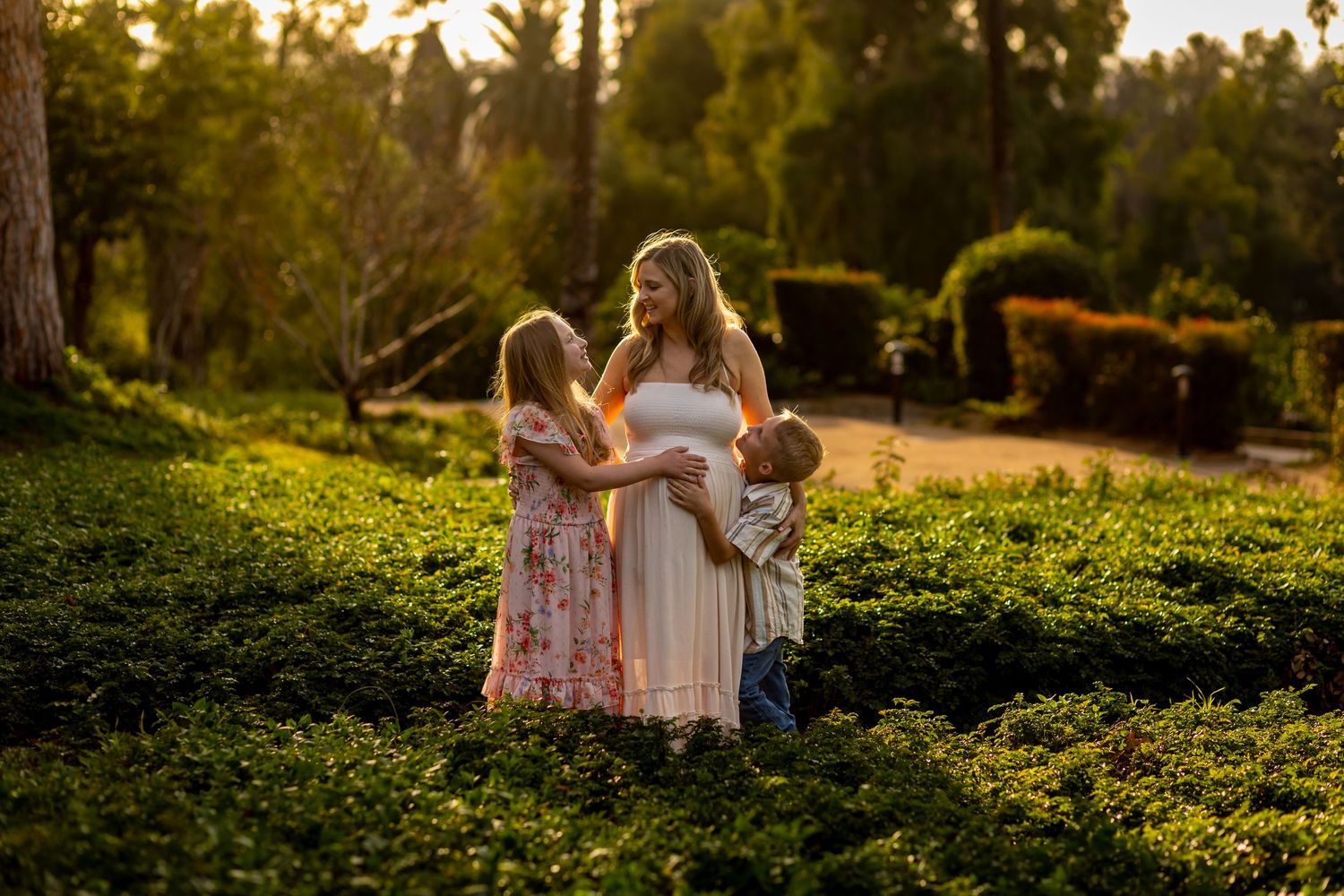 A tender family moment captured in a sunlit garden with children and flowing dresses.