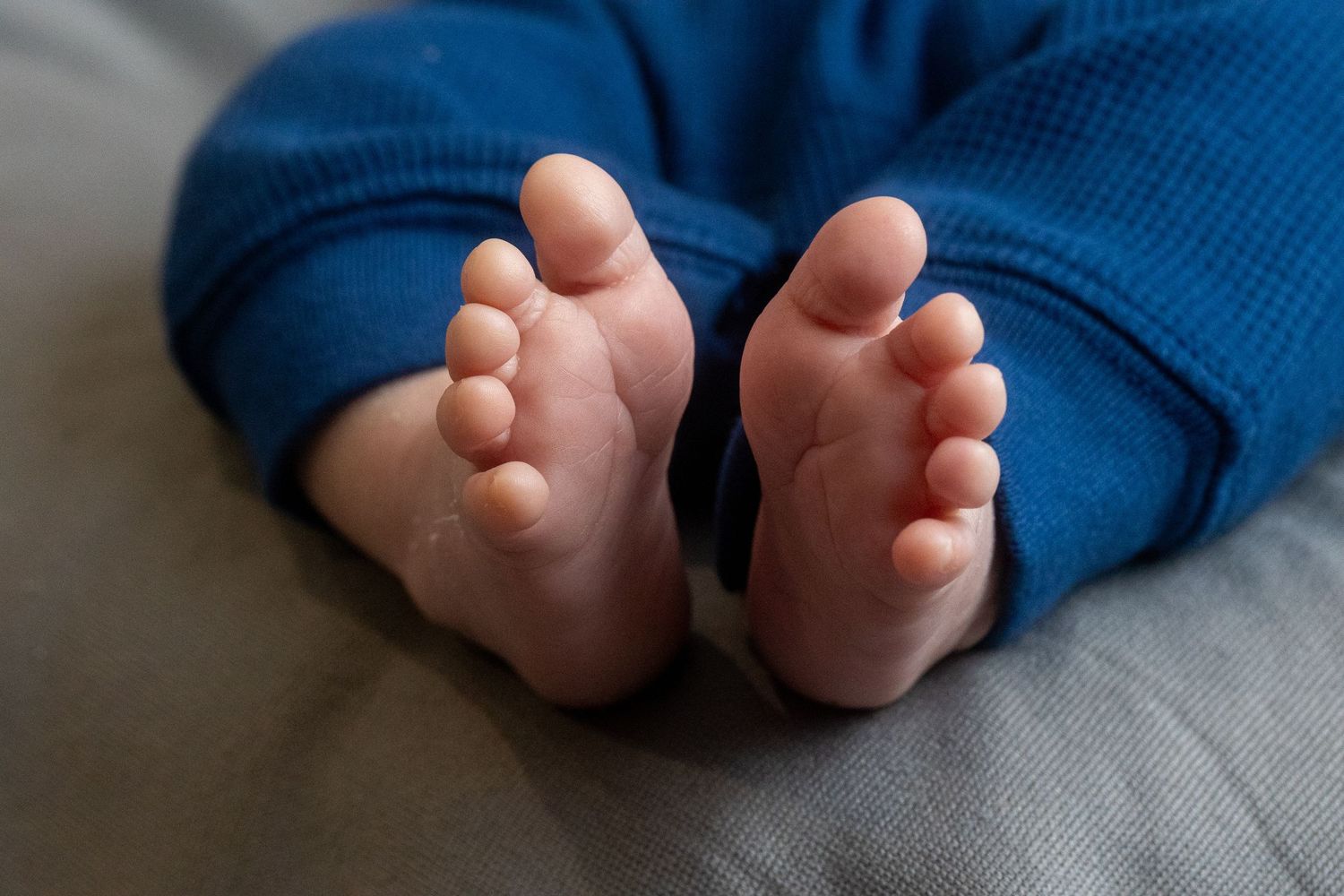 Baby's tiny toes and feet wearing blue clothing against a grey background.