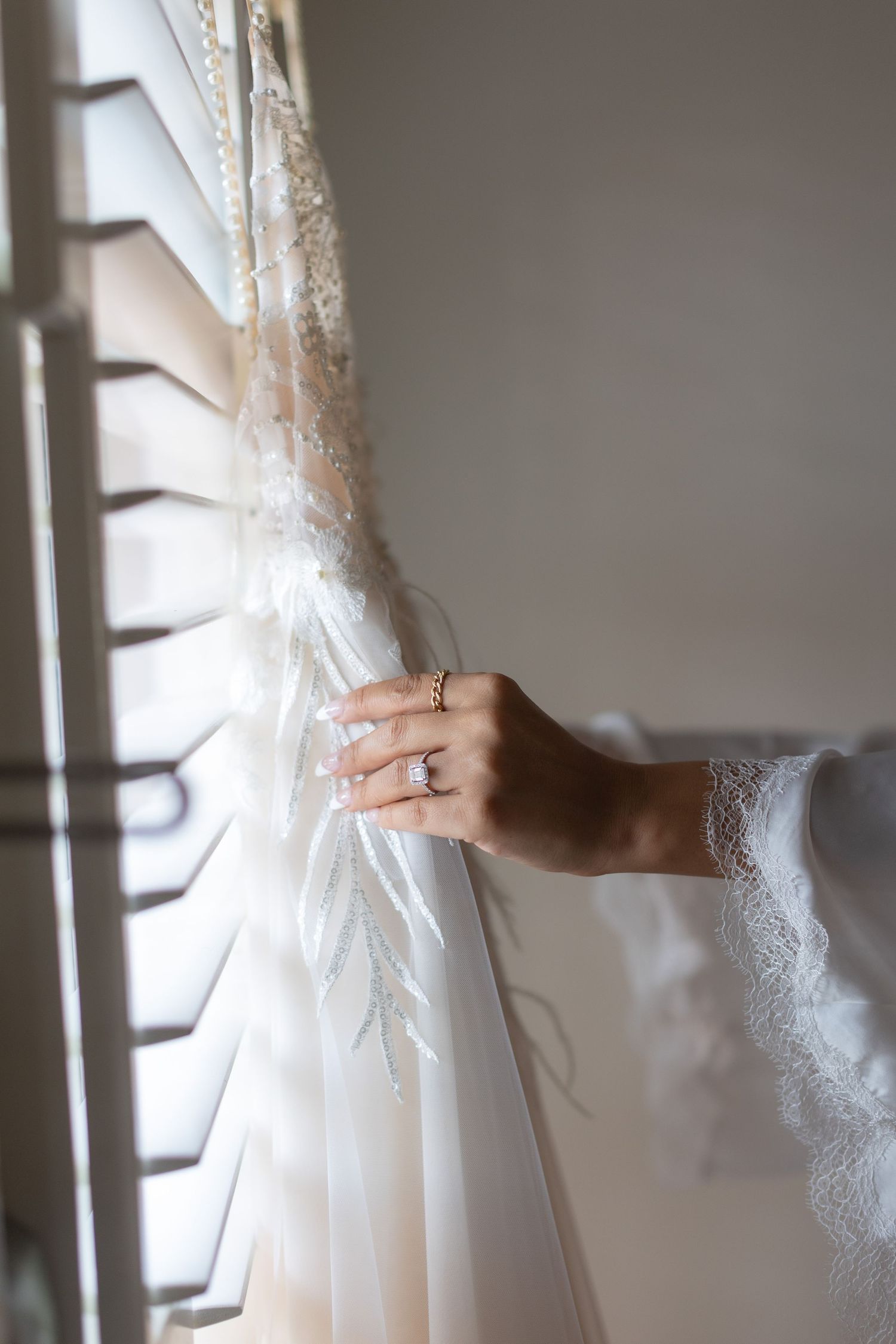 Close-up of lace wedding dress detail with engagement ring visible on hand.