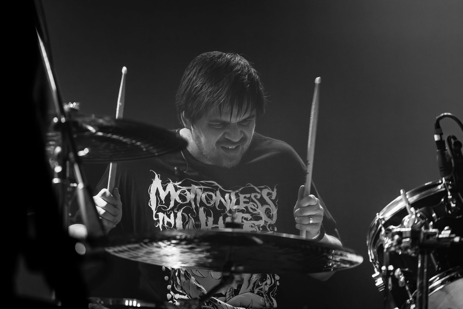 Drummer in black t-shirt performing intensely behind drum kit during concert performance in Pomona