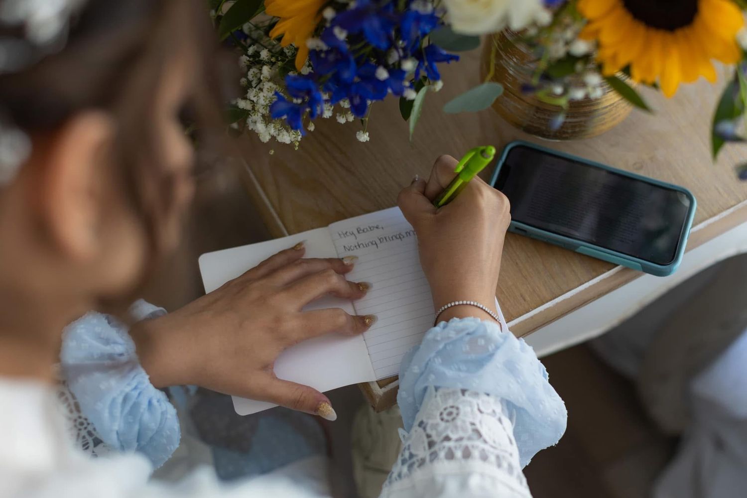 A collection of wedding setting details including sunflowers, blue flowers, and writing on paper at a decorated table.