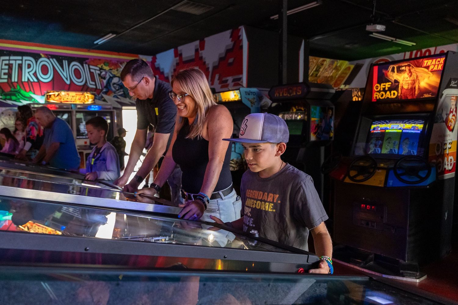 Dark arcade interior with illuminated game machines and neon signs creating ambient lighting.