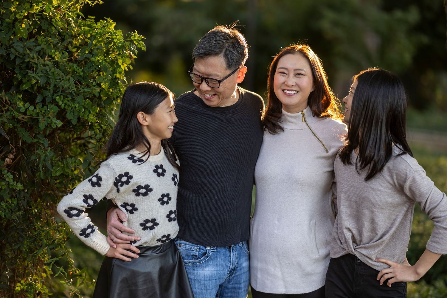 Family of four poses outdoors together during autumn season with warm lighting.