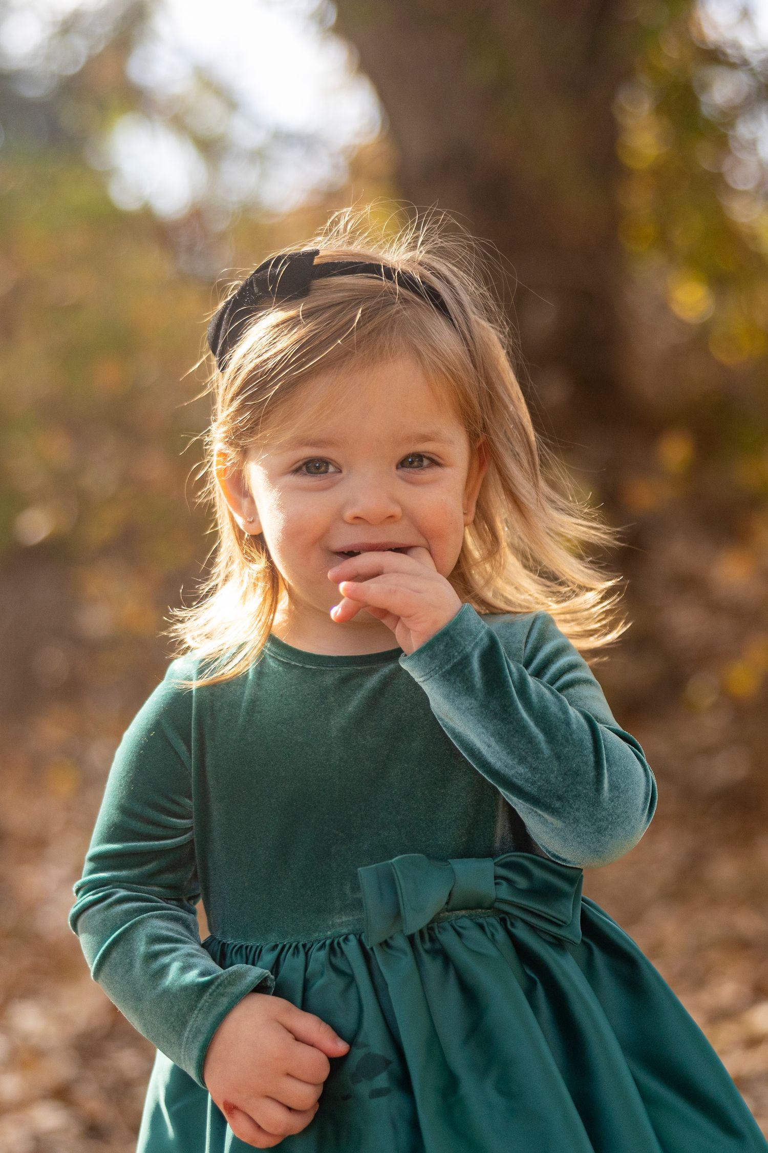 A young child in a green dress giggles during an autumn photo session.