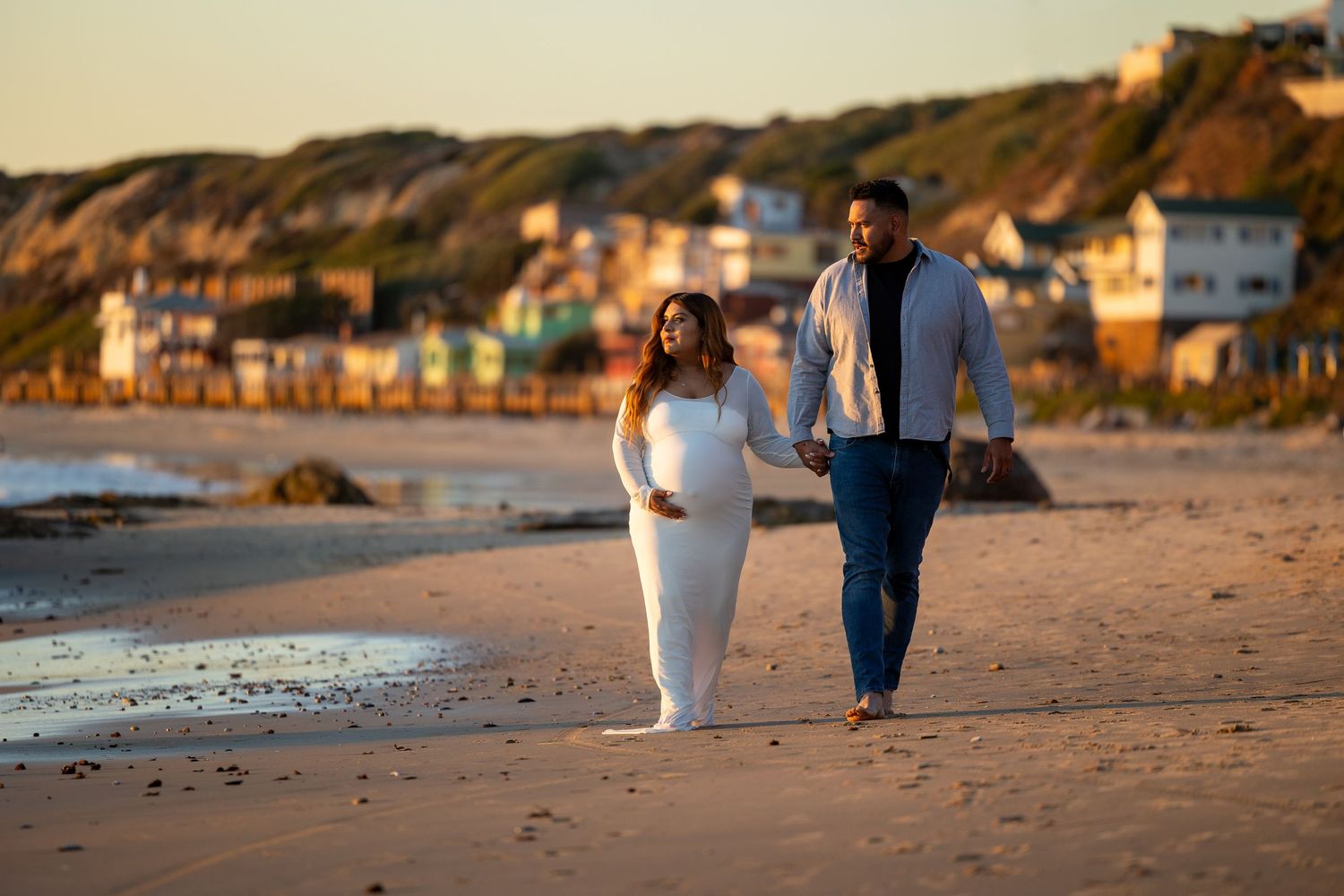 A couple walking along a scenic beach at sunset with coastal homes and cliffs in the background in Huntington Beach.