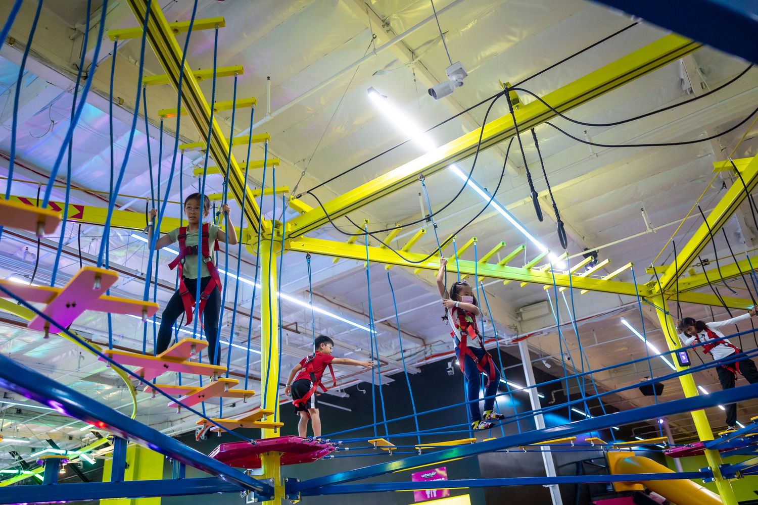 Colorful ropes course and climbing equipment suspended from ceiling in indoor recreation facility.