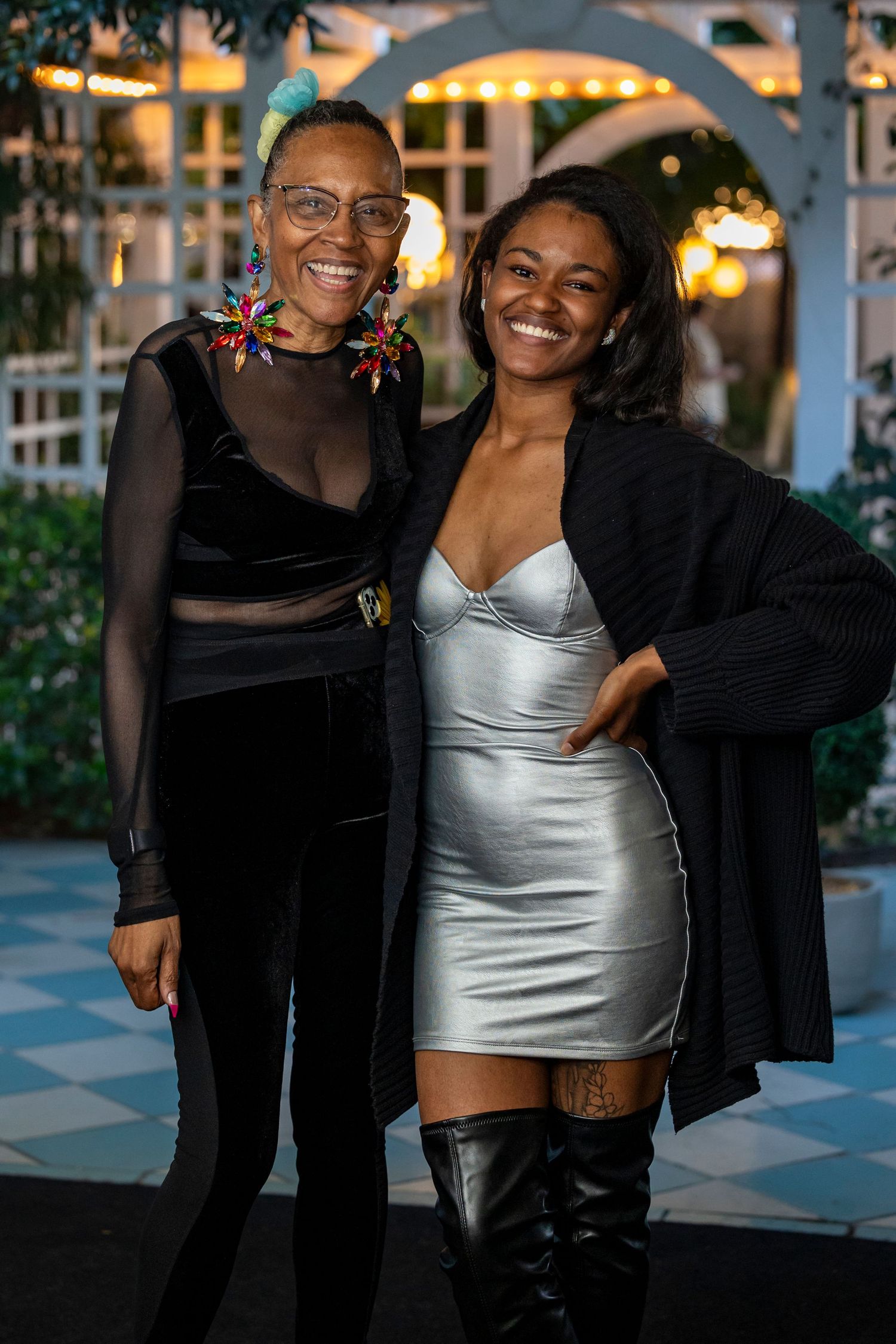 Evening event attendees in formal attire posing outdoors with decorative lighting.