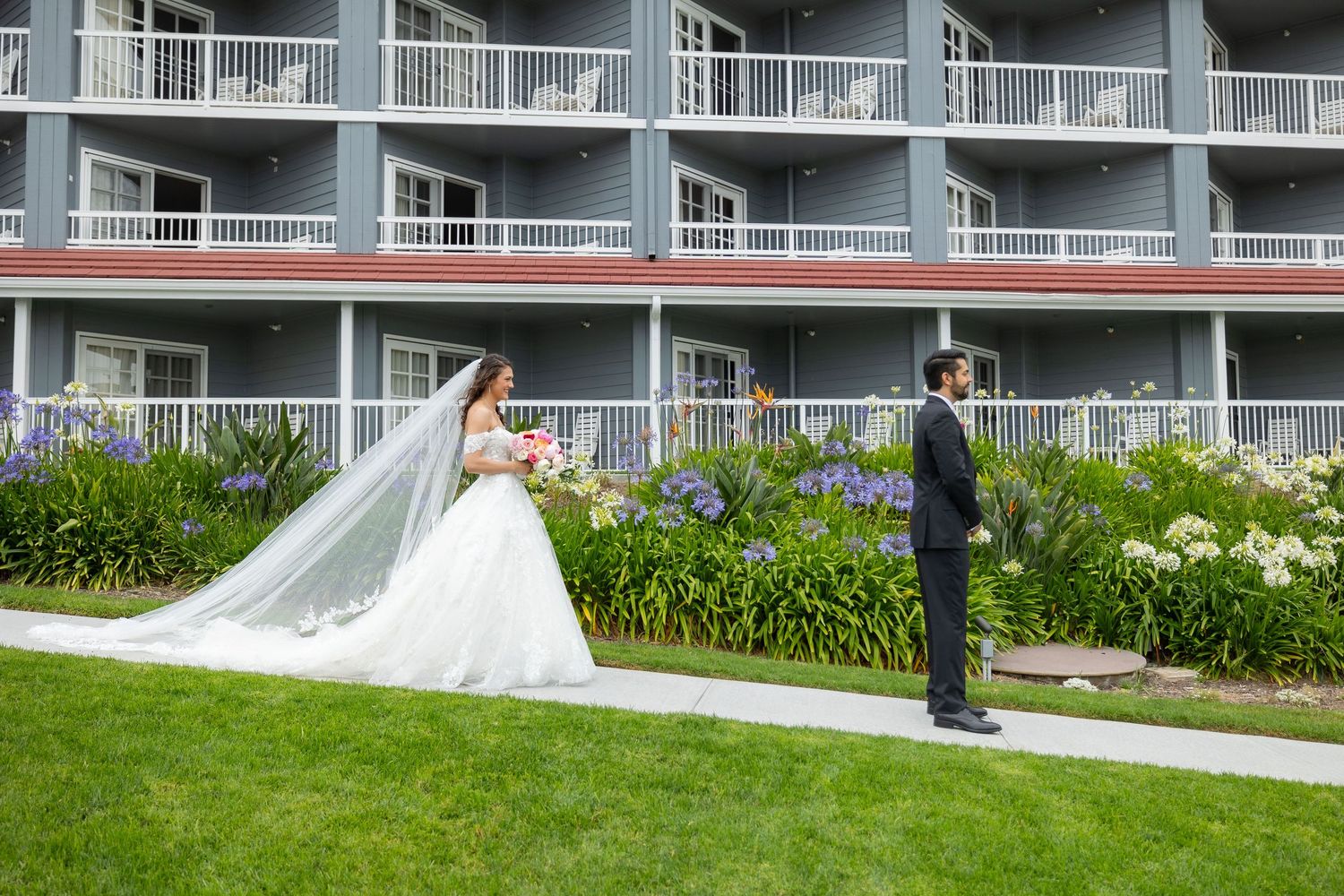 Wedding photos being taken on a bright green lawn outside a multi-story waterfront resort building with white balconies.