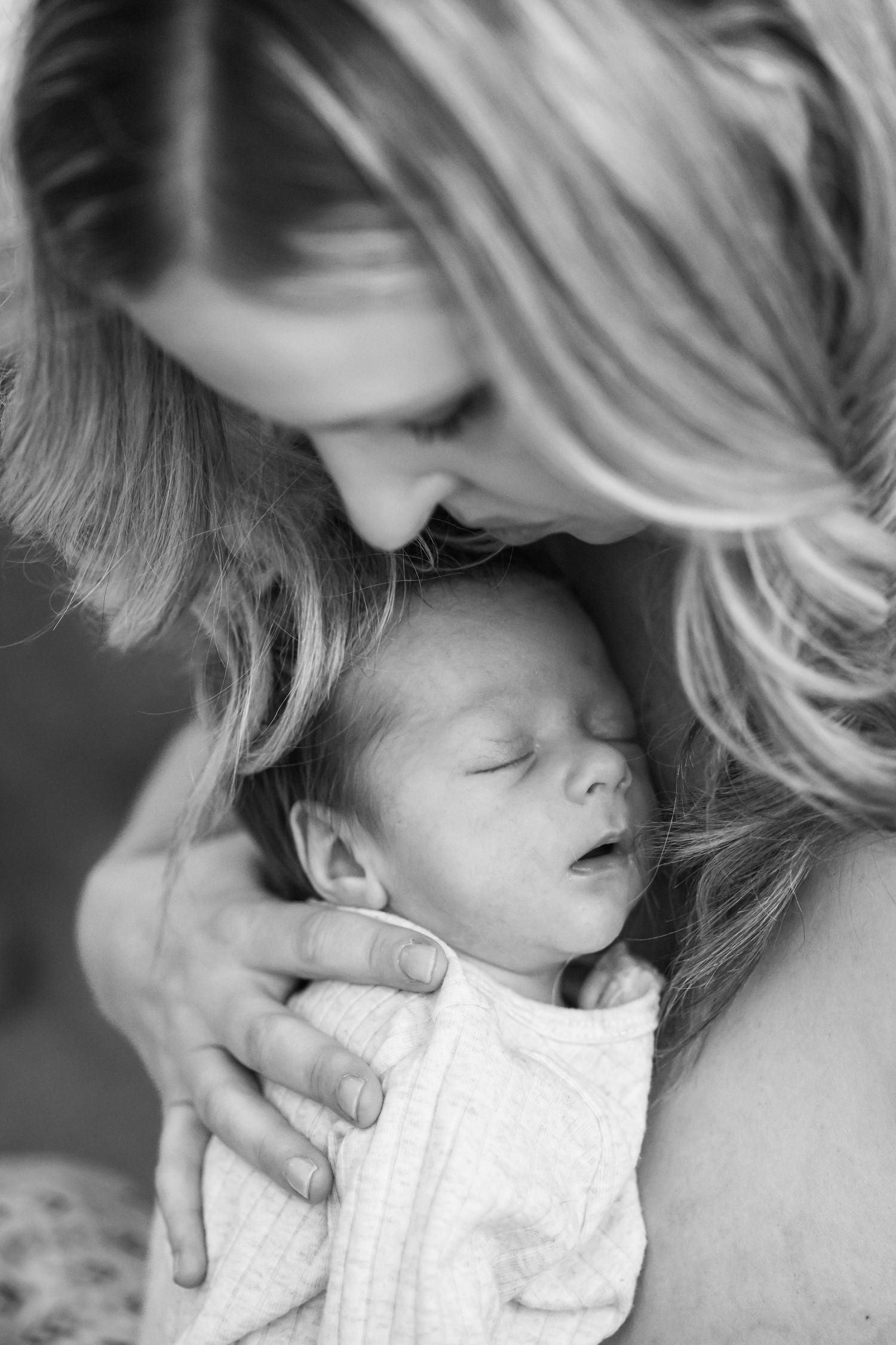 A tender black and white portrait of a mother cradling her sleeping newborn baby against her chest at home in Beaumont