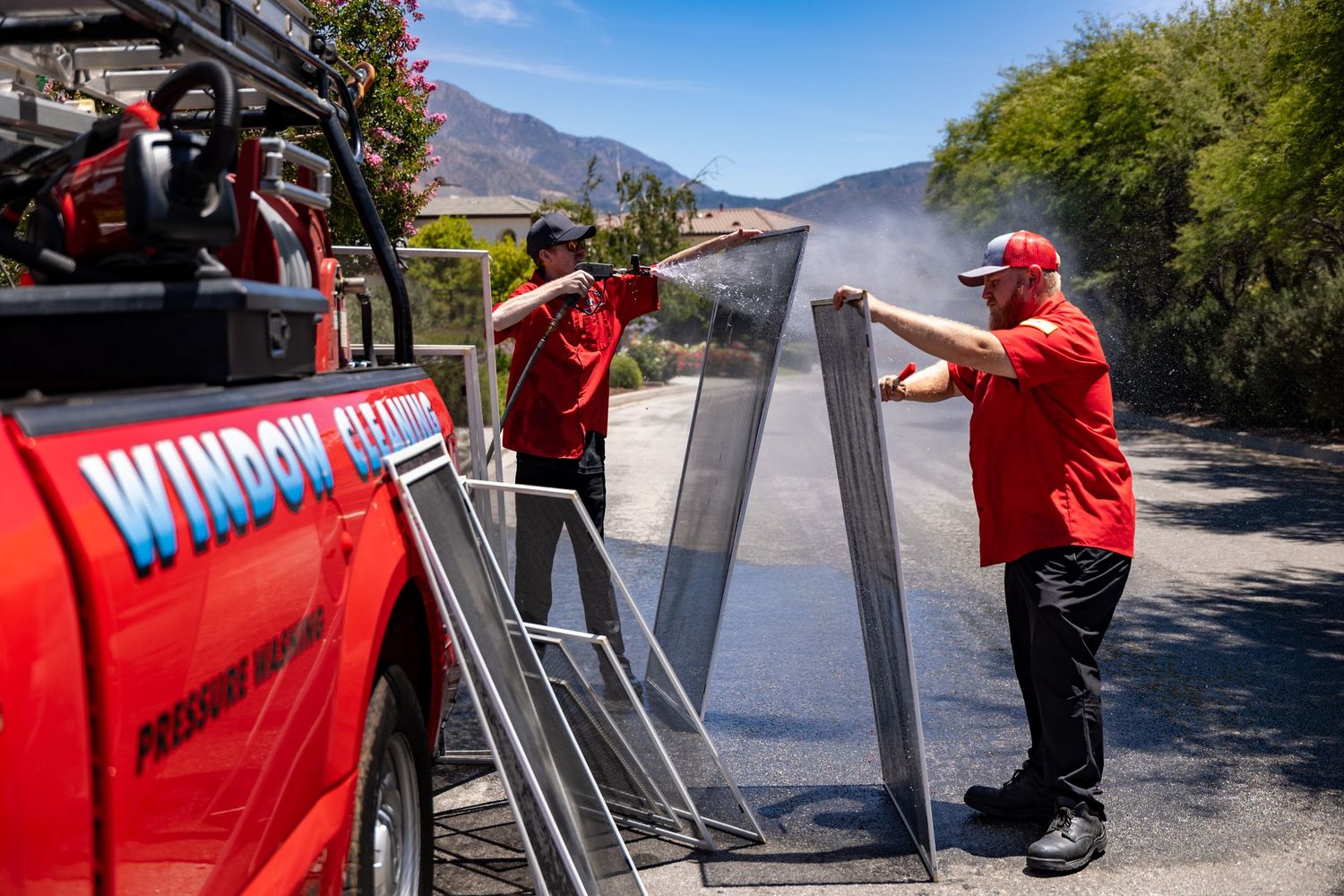 Workers in red uniforms install metal posts along a mountain road for safety improvements during sunny weather.