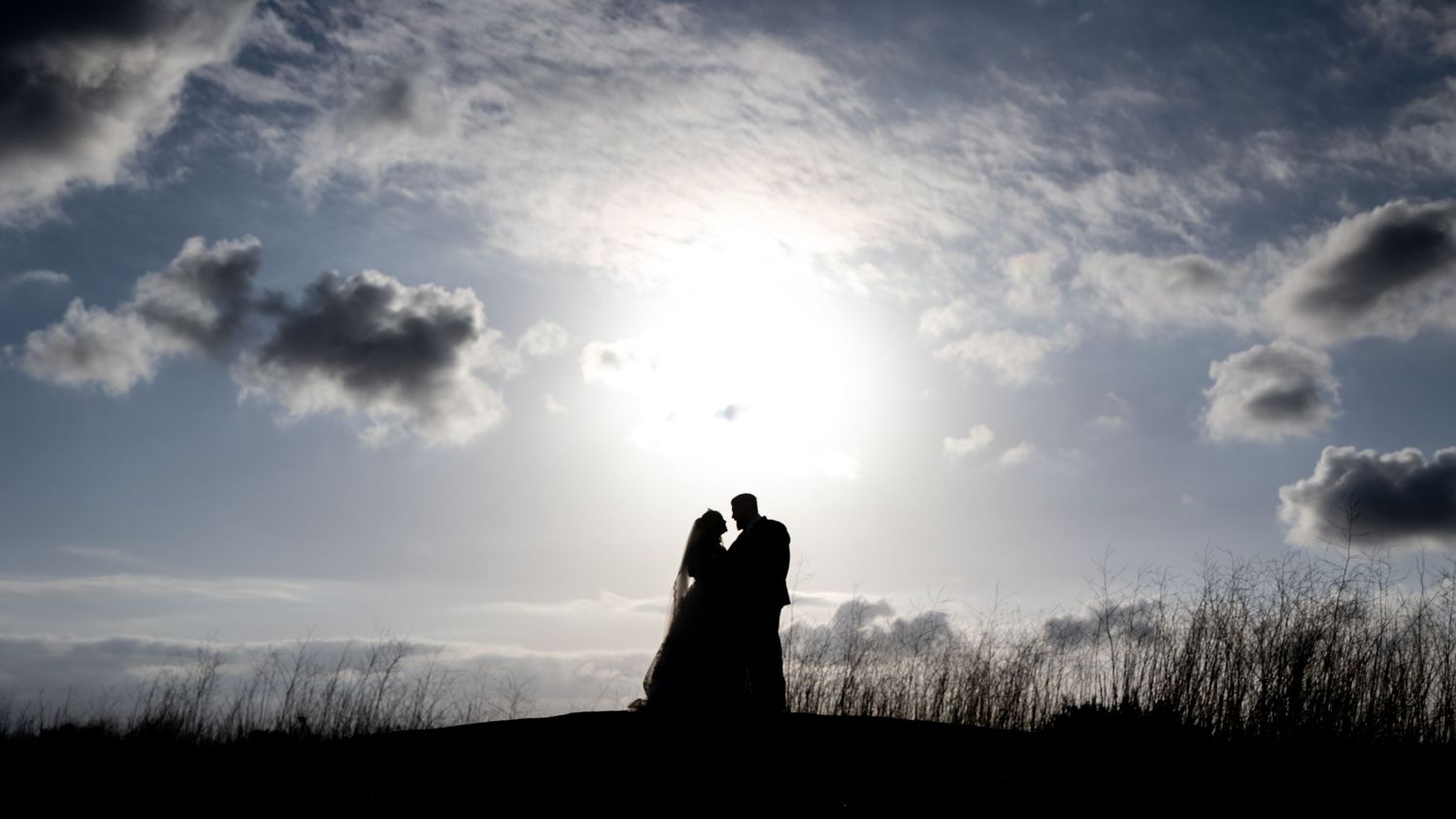 Silhouetted couple against dramatic sunset sky with dark clouds.