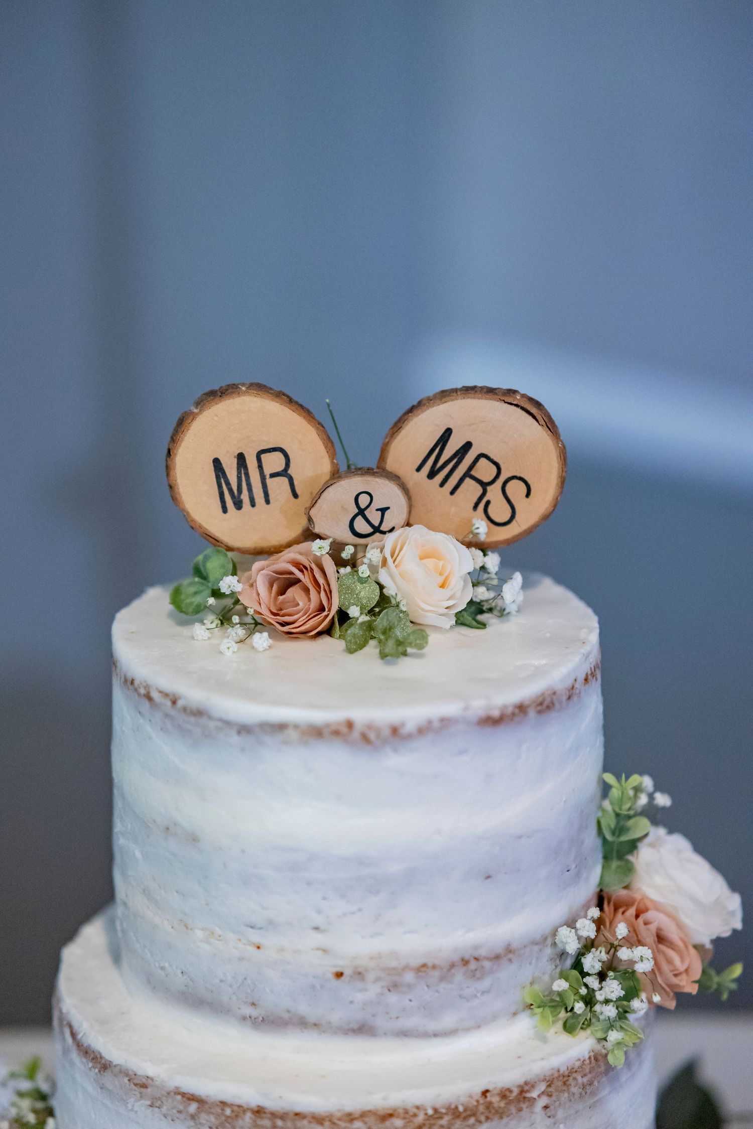 Rustic wedding cake with wooden Mr & Mrs toppers decorated with pink roses and greenery.