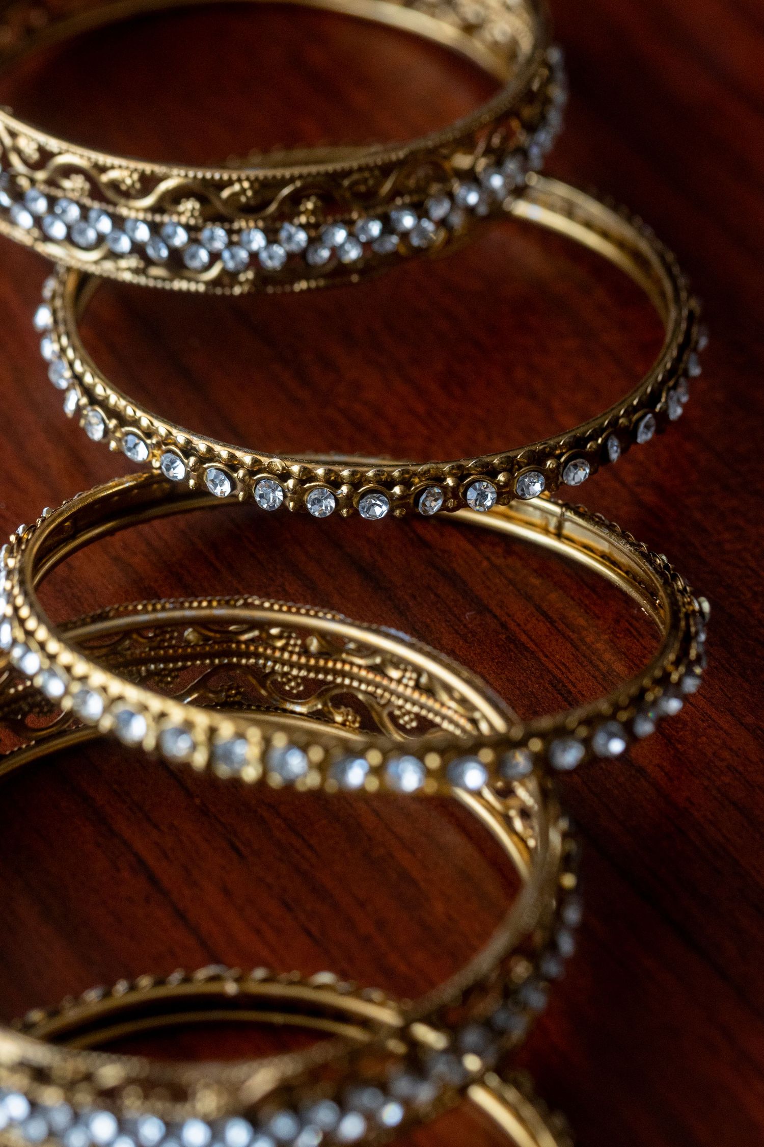 Vintage-style gold bangles with crystal accents arranged in a decorative pattern on dark wood.