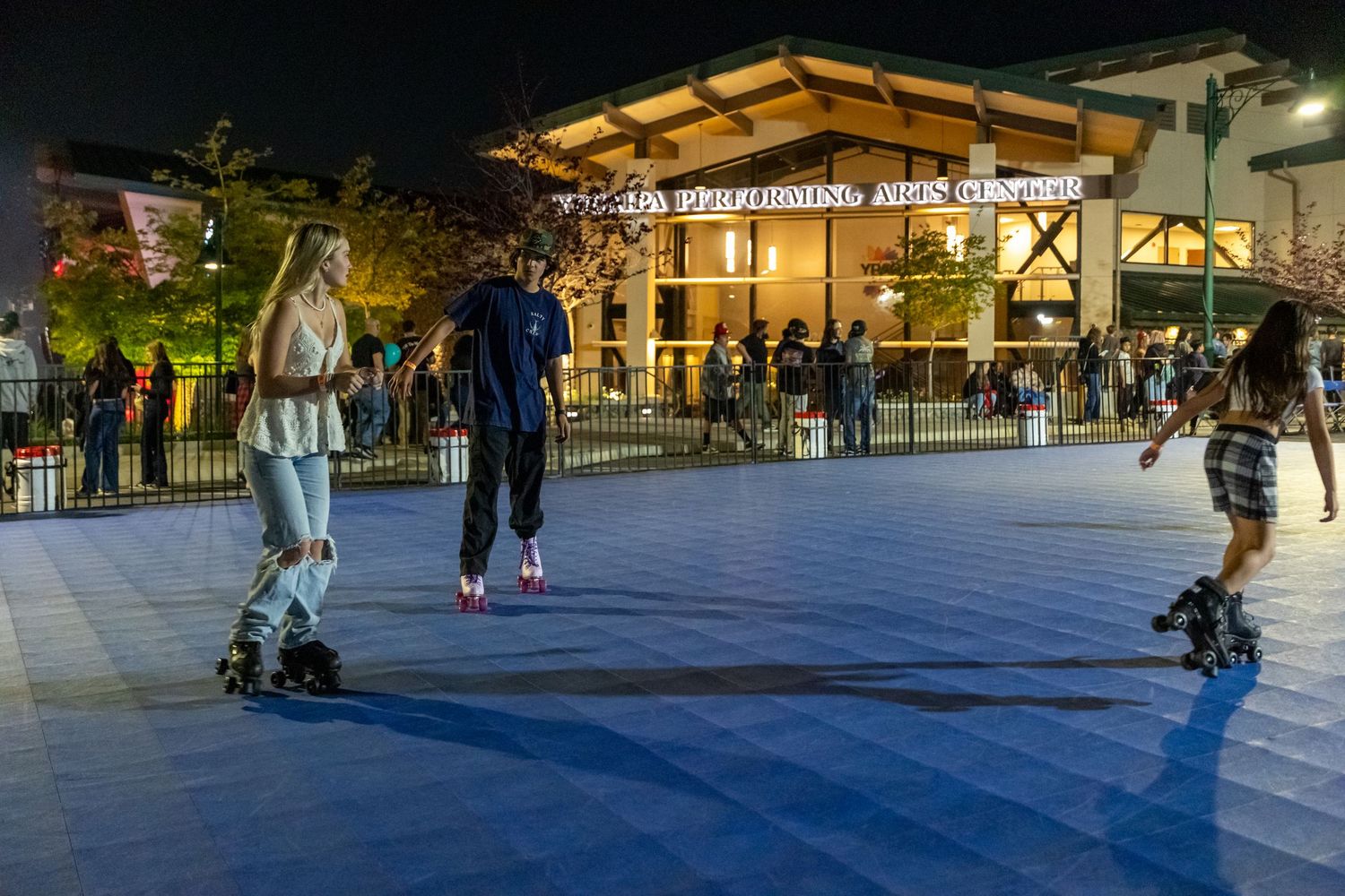 People roller skating at night outside an illuminated building.