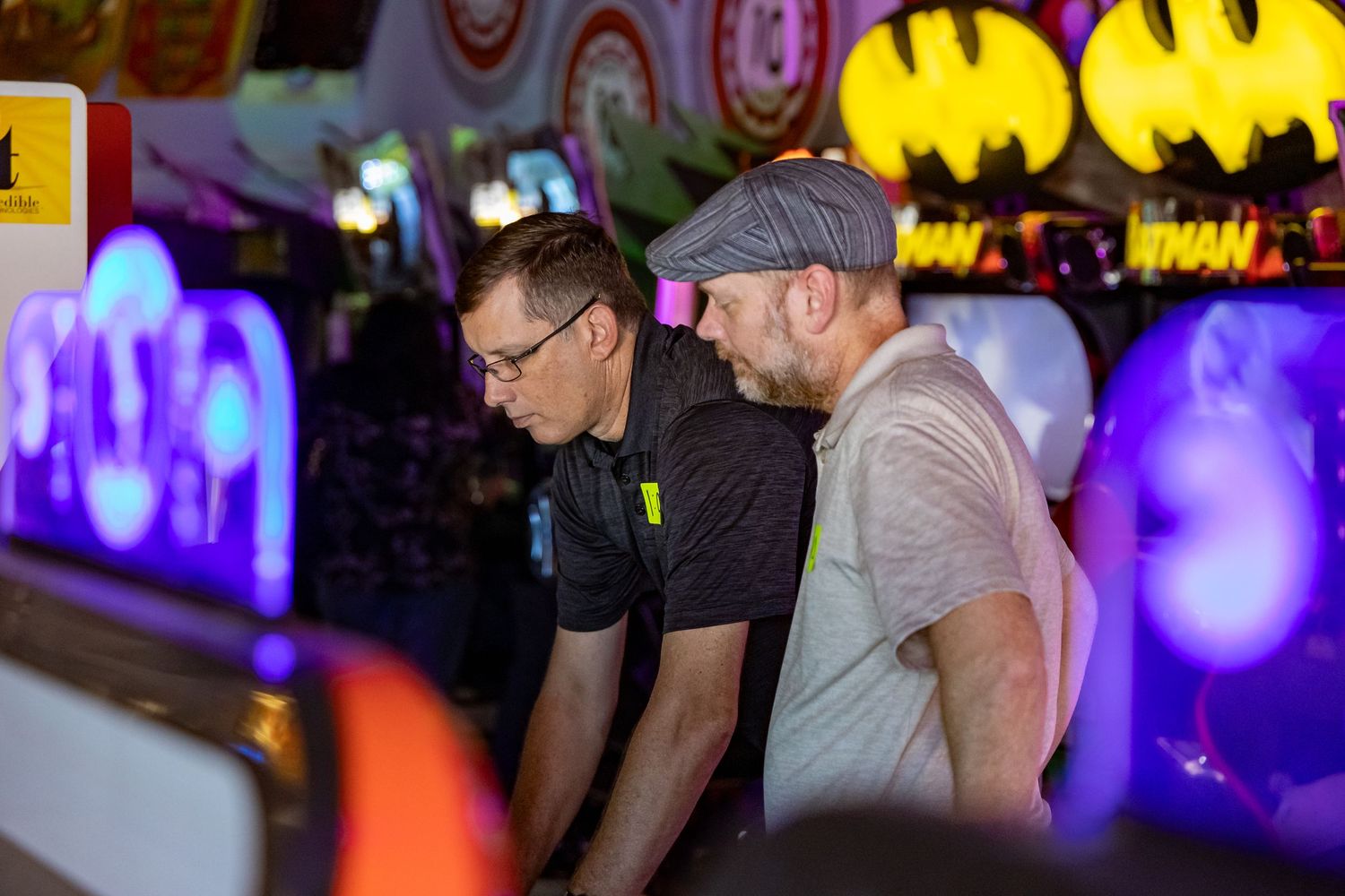 Players engage with classic arcade games in a dimly lit room with vibrant neon signage.
