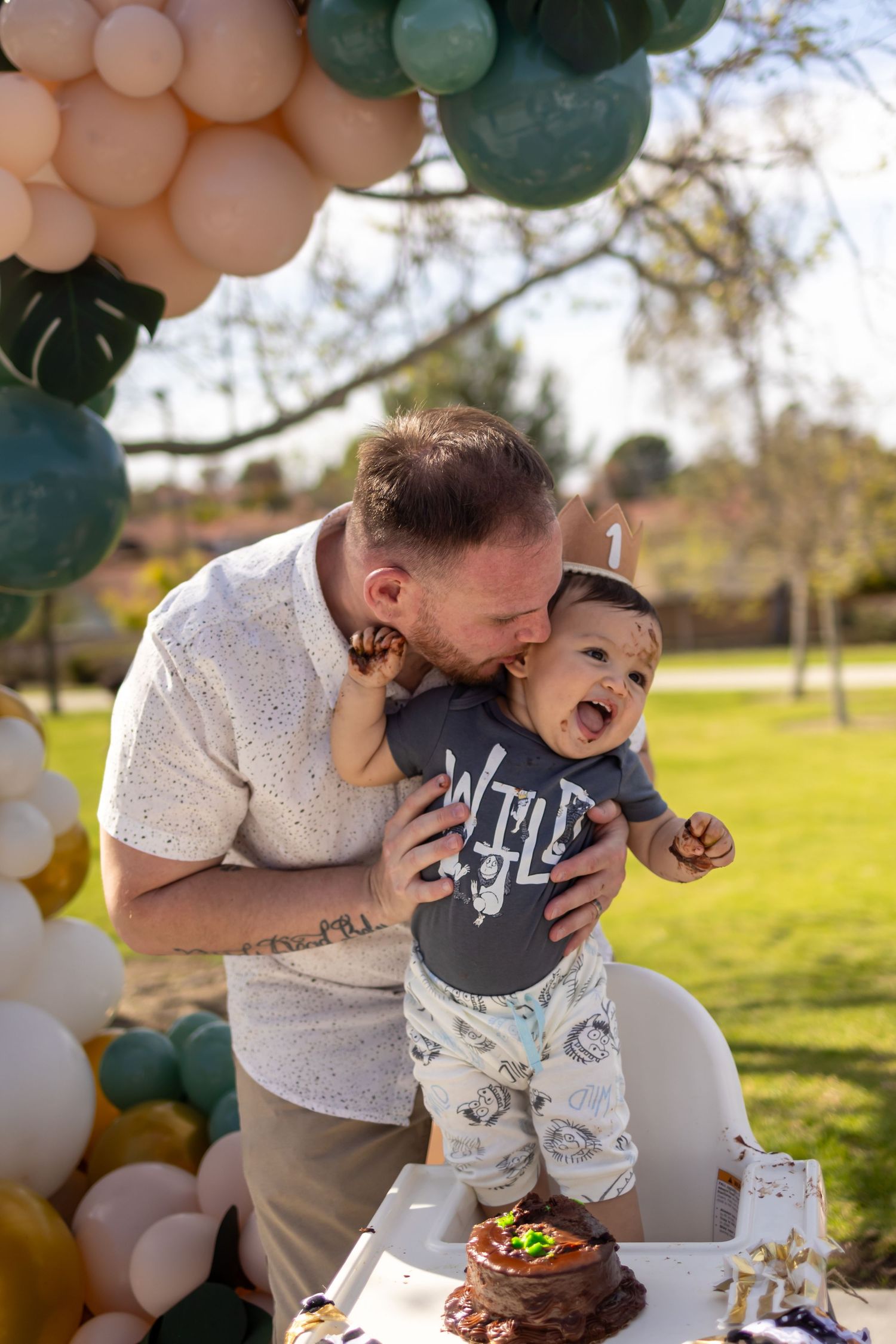 Father and baby sharing a playful moment at decorated outdoor birthday party.