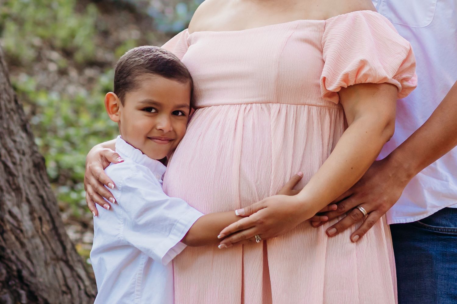 A touching family maternity moment with a pink dress in natural lighting.