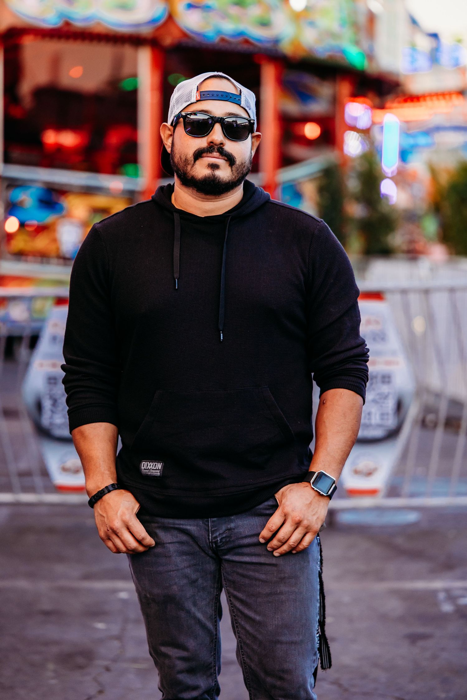 A casually dressed person in black attire and sunglasses poses outdoors on blurred city streets.