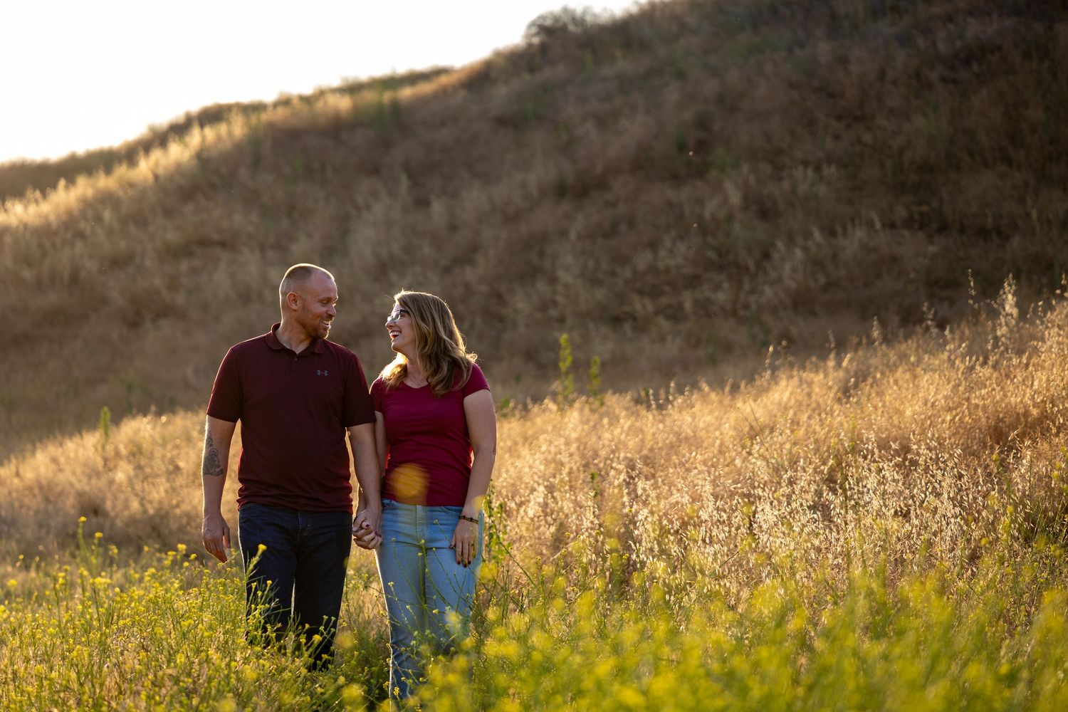 A couple walking through golden wildflowers on a hillside at sunset.