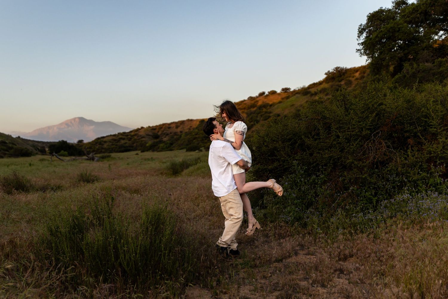 A playful couple enjoying a sunset moment in a mountainous field.