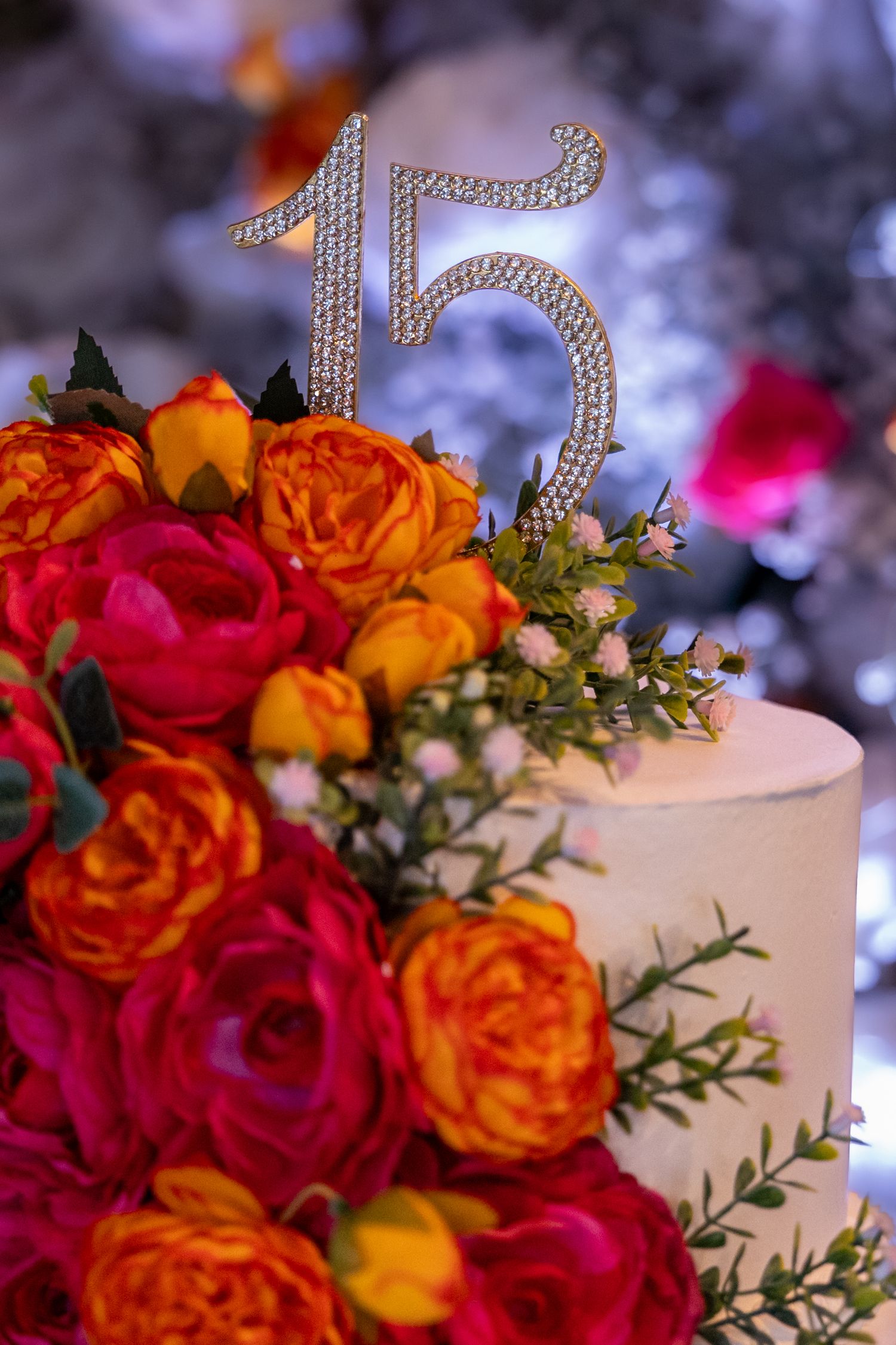 A decorative number 15 cake topper adorned with orange and pink roses on a white cake.