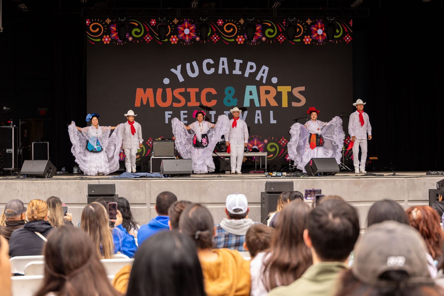 Dance performance at Yucaipa Music & Arts Festival with dancers in traditional white costumes on stage.