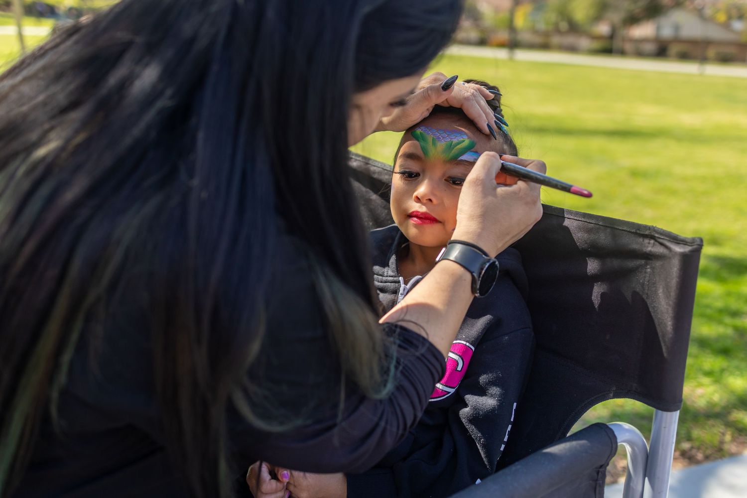 Makeup artist applying colorful eyeshadow on a client outdoors in natural lighting.