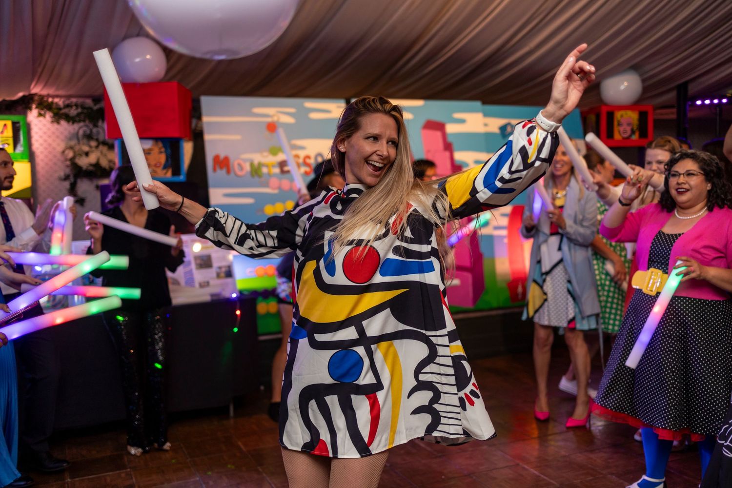 People in colorful outfits dancing and enjoying themselves at an indoor party with balloon decorations.