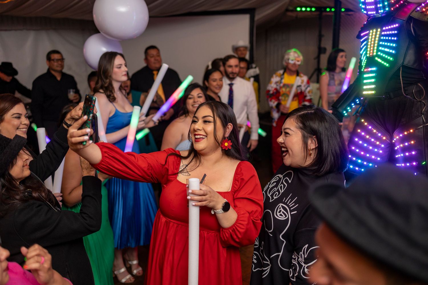 Guests dancing and celebrating at a lively party with colorful LED lights and decorations in the background.
