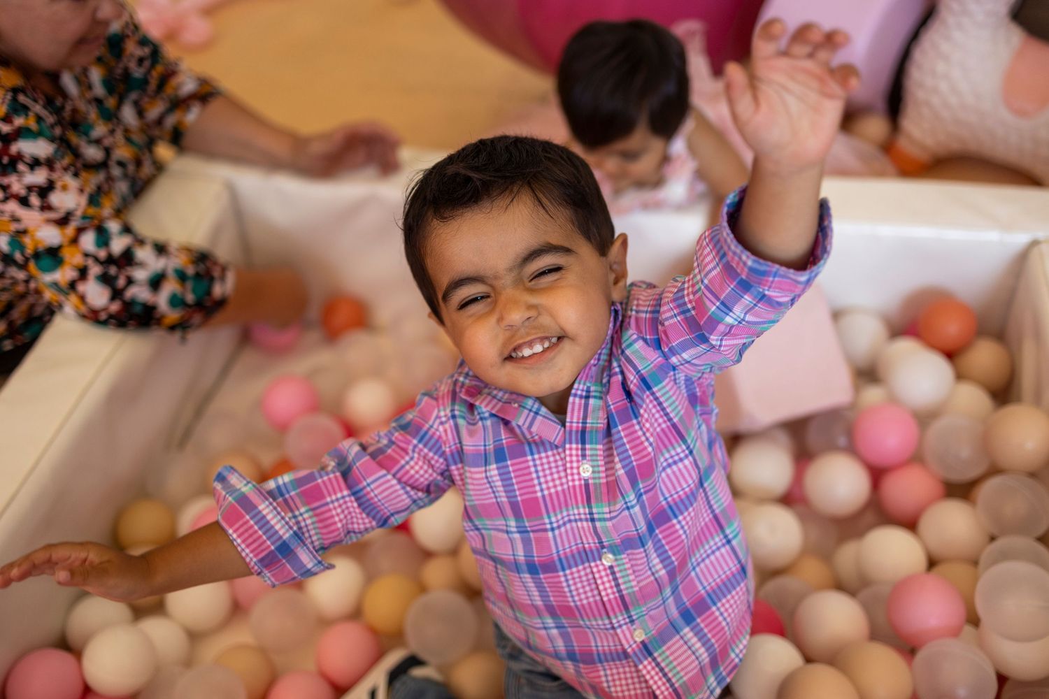 Child in plaid shirt playing in a ball pit with colorful plastic spheres in Riverside.