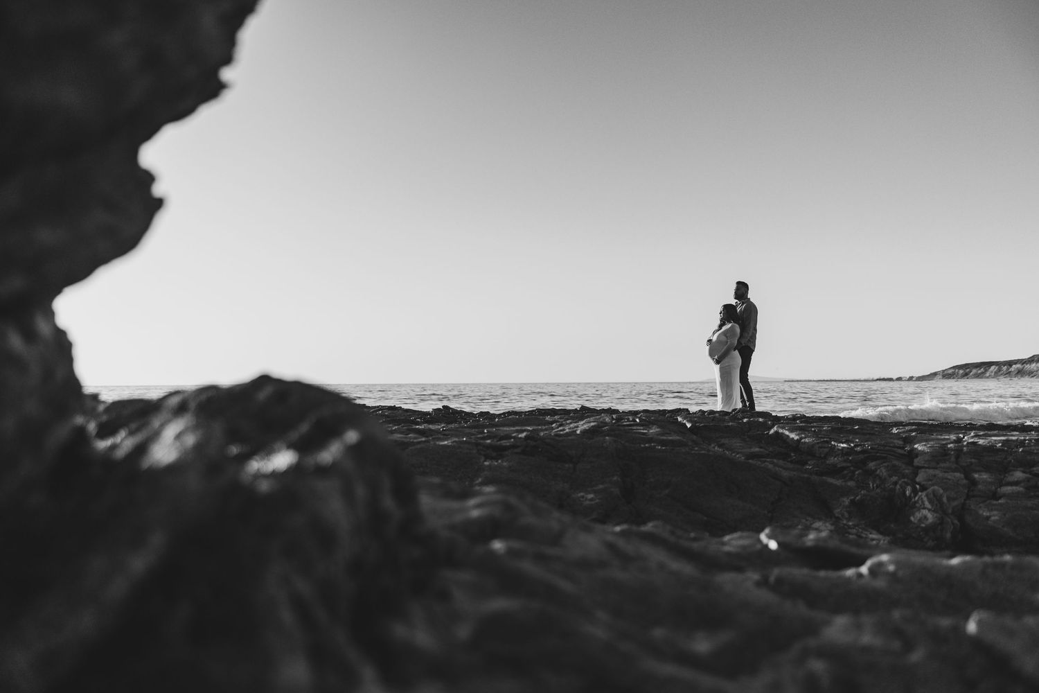 Black and white coastal landscape with silhouetted figures on rocky cliffs.