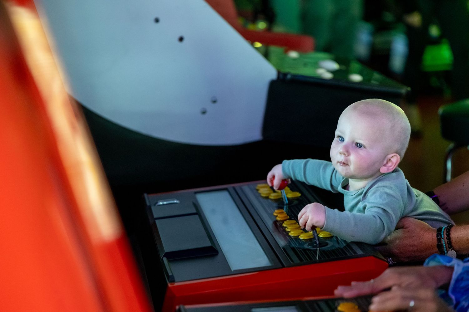 Young player engages with arcade game cabinet in colorful lighting.