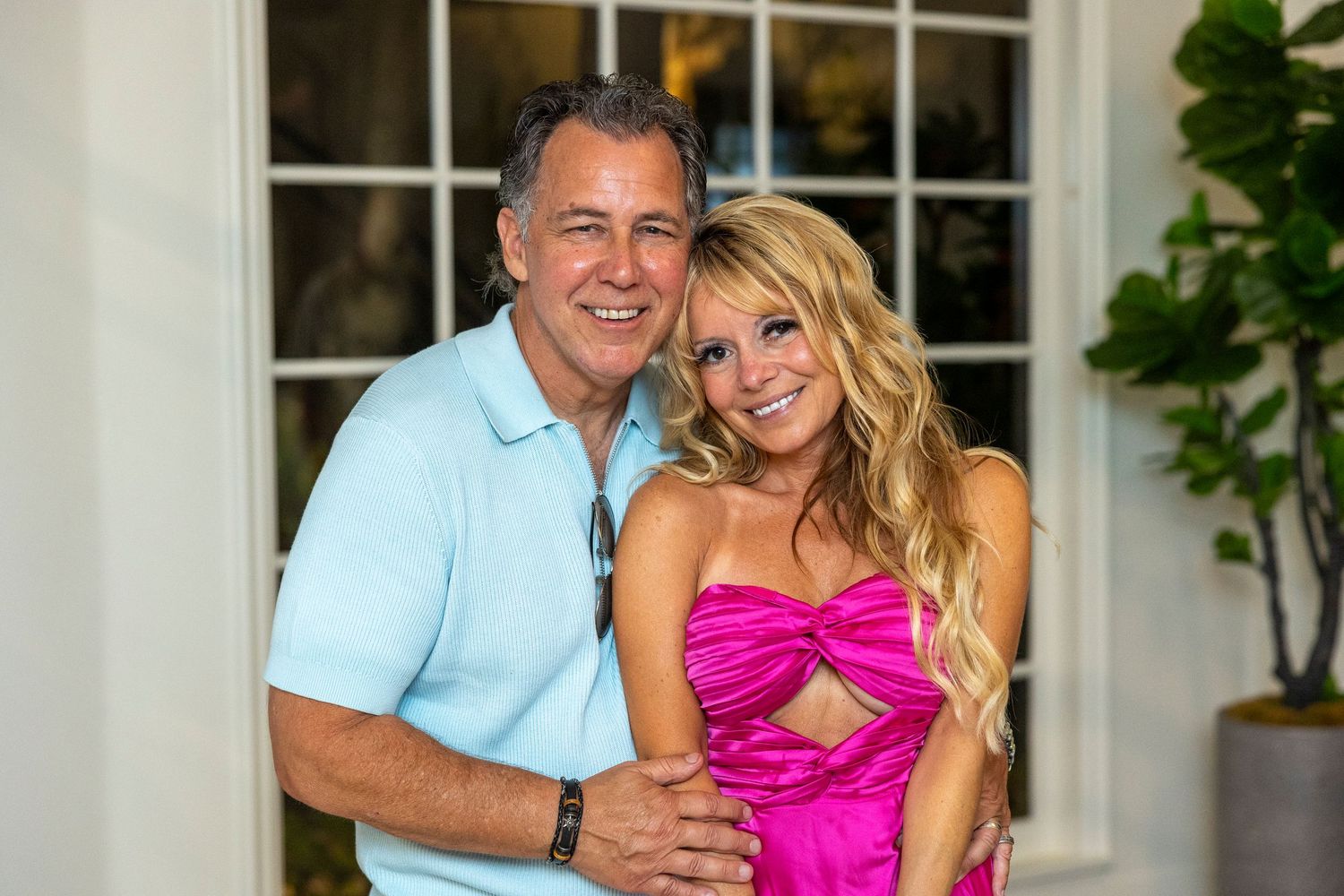 Couple posing together against white exterior of building.