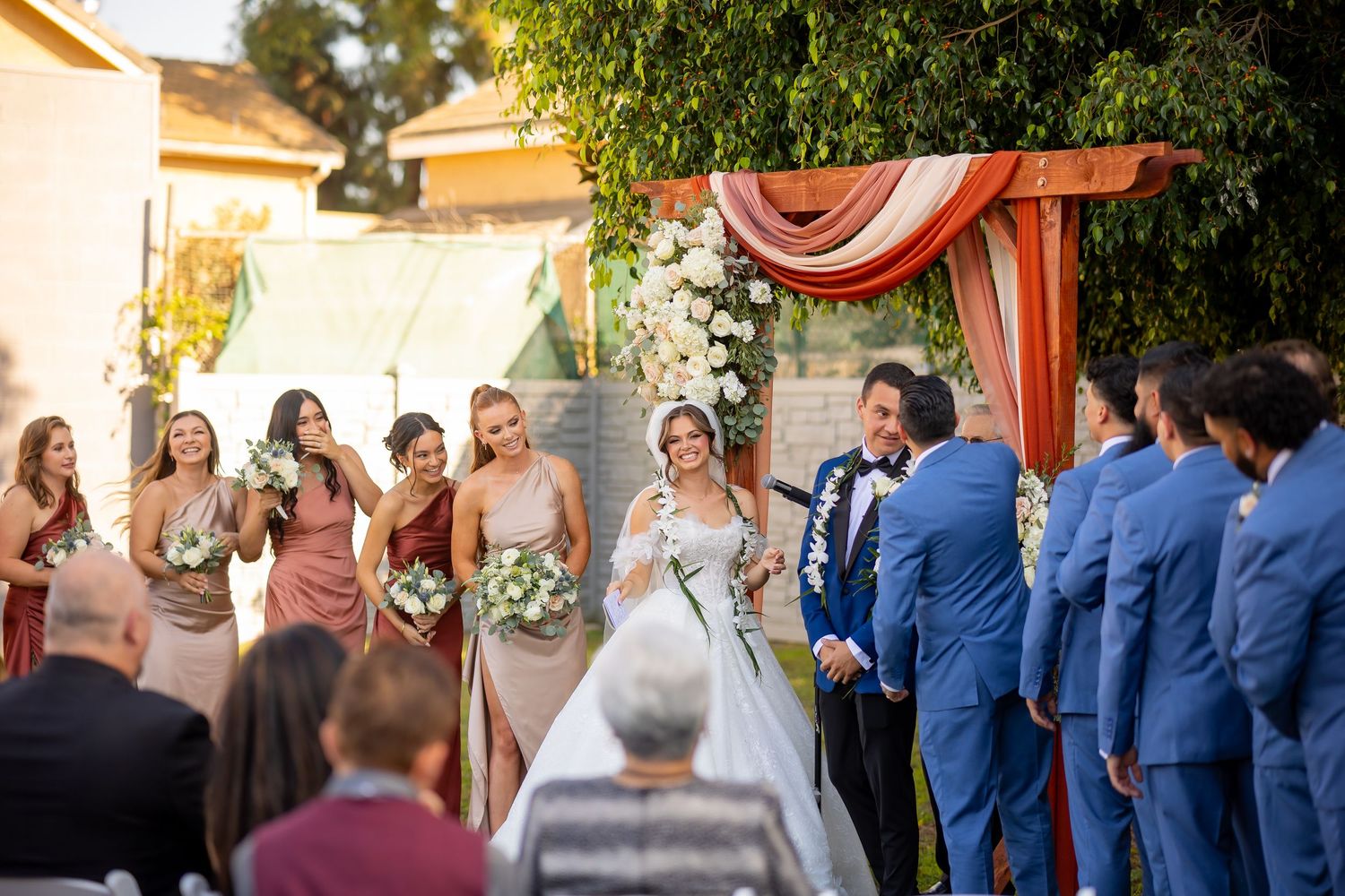 Wedding party members in blue and black attire standing in an outdoor venue.