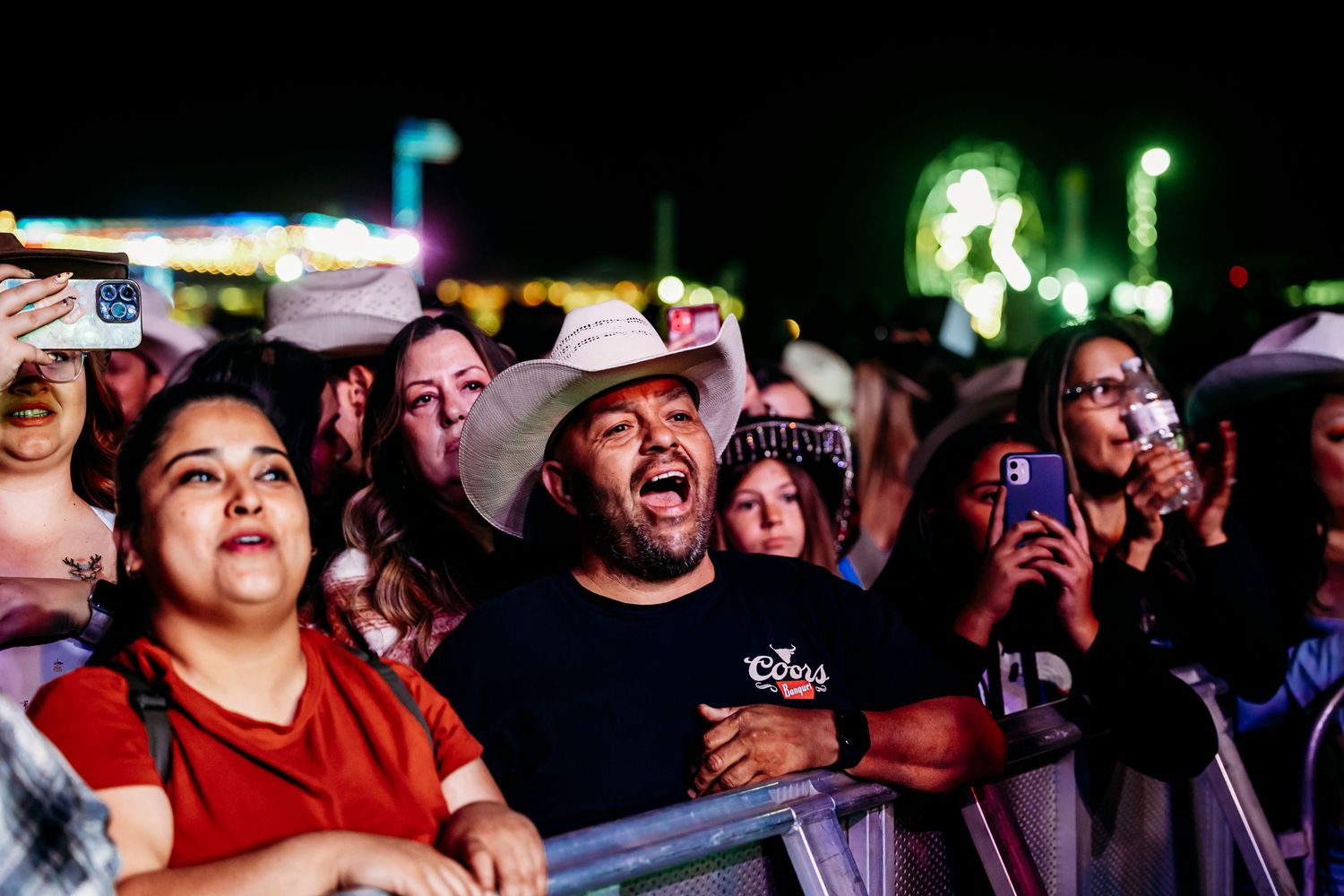 Enthusiastic crowd of concertgoers in cowboy hats cheering at an outdoor country music festival.
