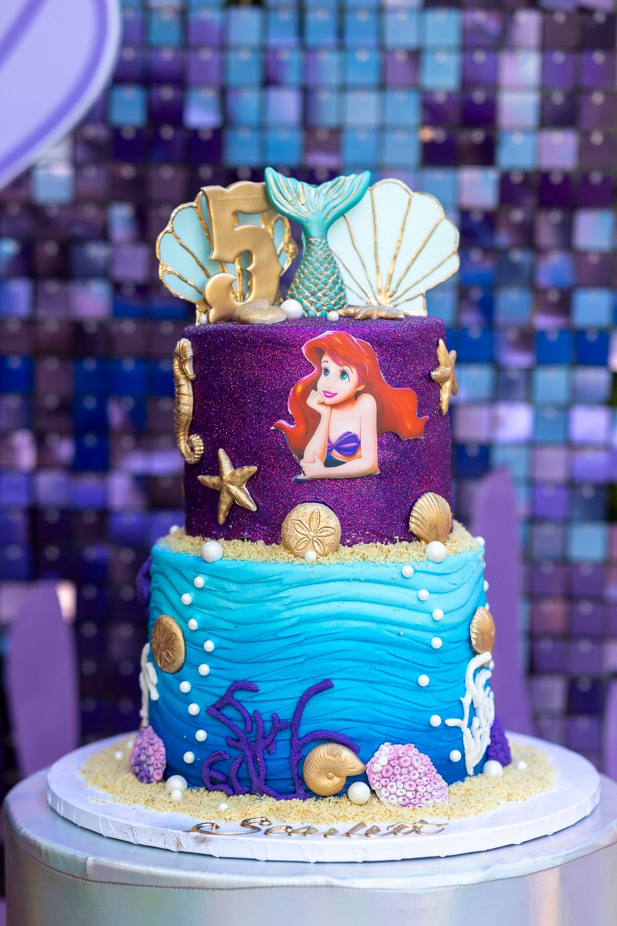 Under the sea themed cake with mermaid decorations, shells, and ocean waves in purple and blue fondant.