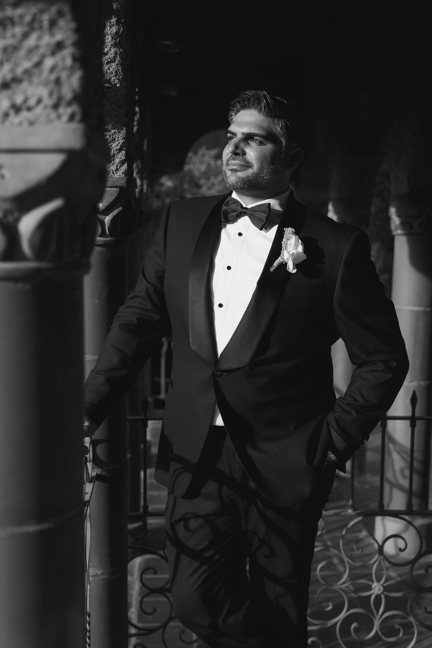 A groom in classic black tuxedo poses elegantly against ornate architecture.