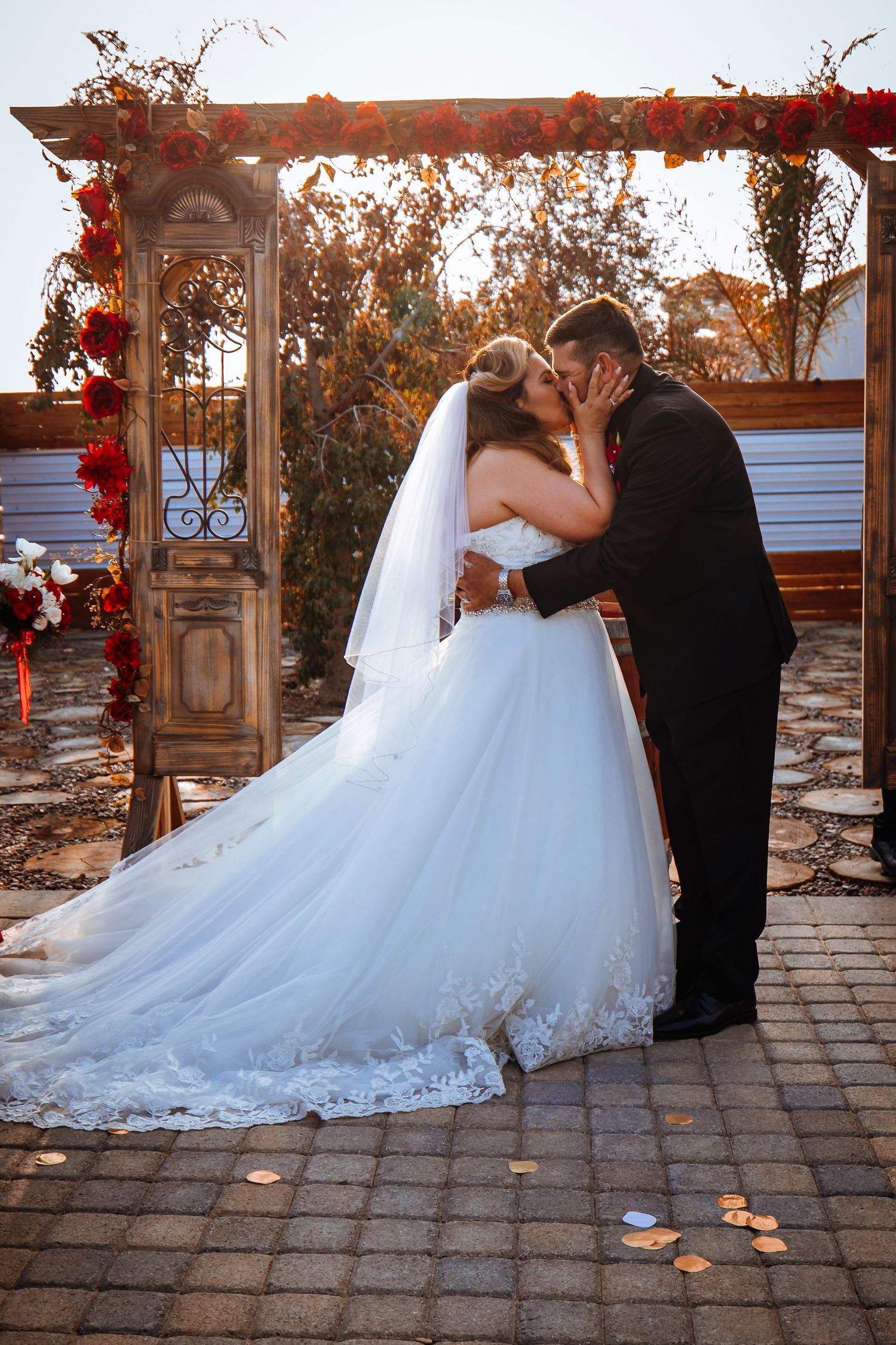 Romantic kiss under floral arch at sunset wedding ceremony.