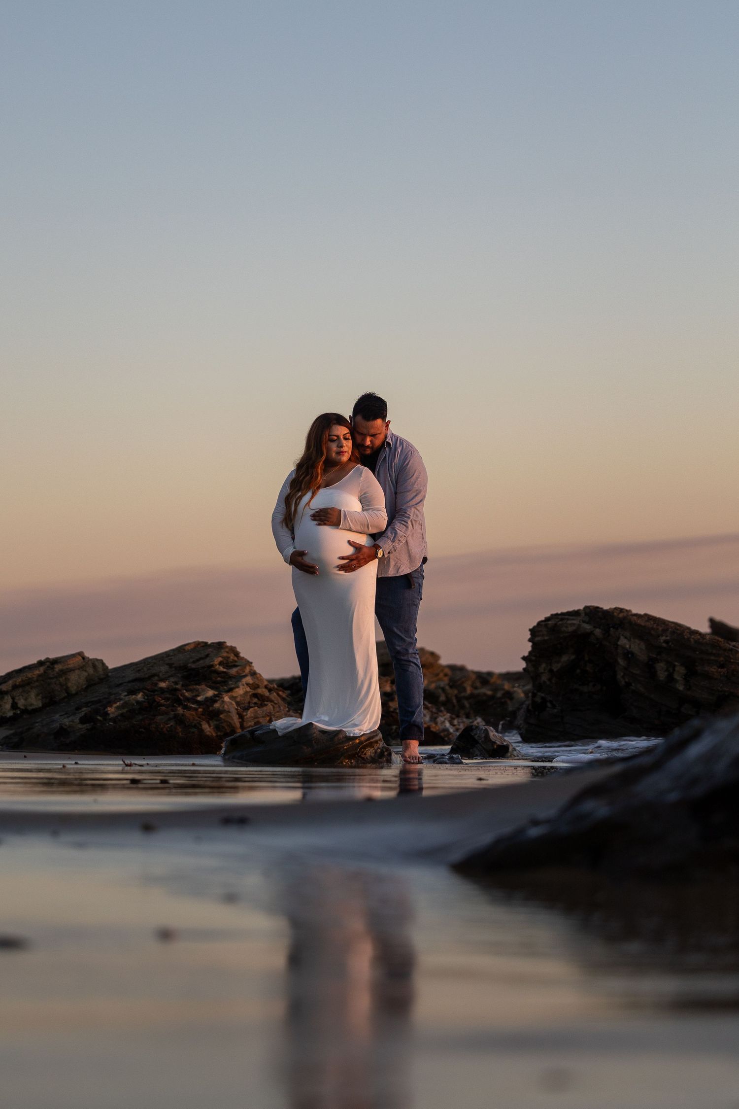 Tranquil beach scene with reflective water pools among rocks at sunset.