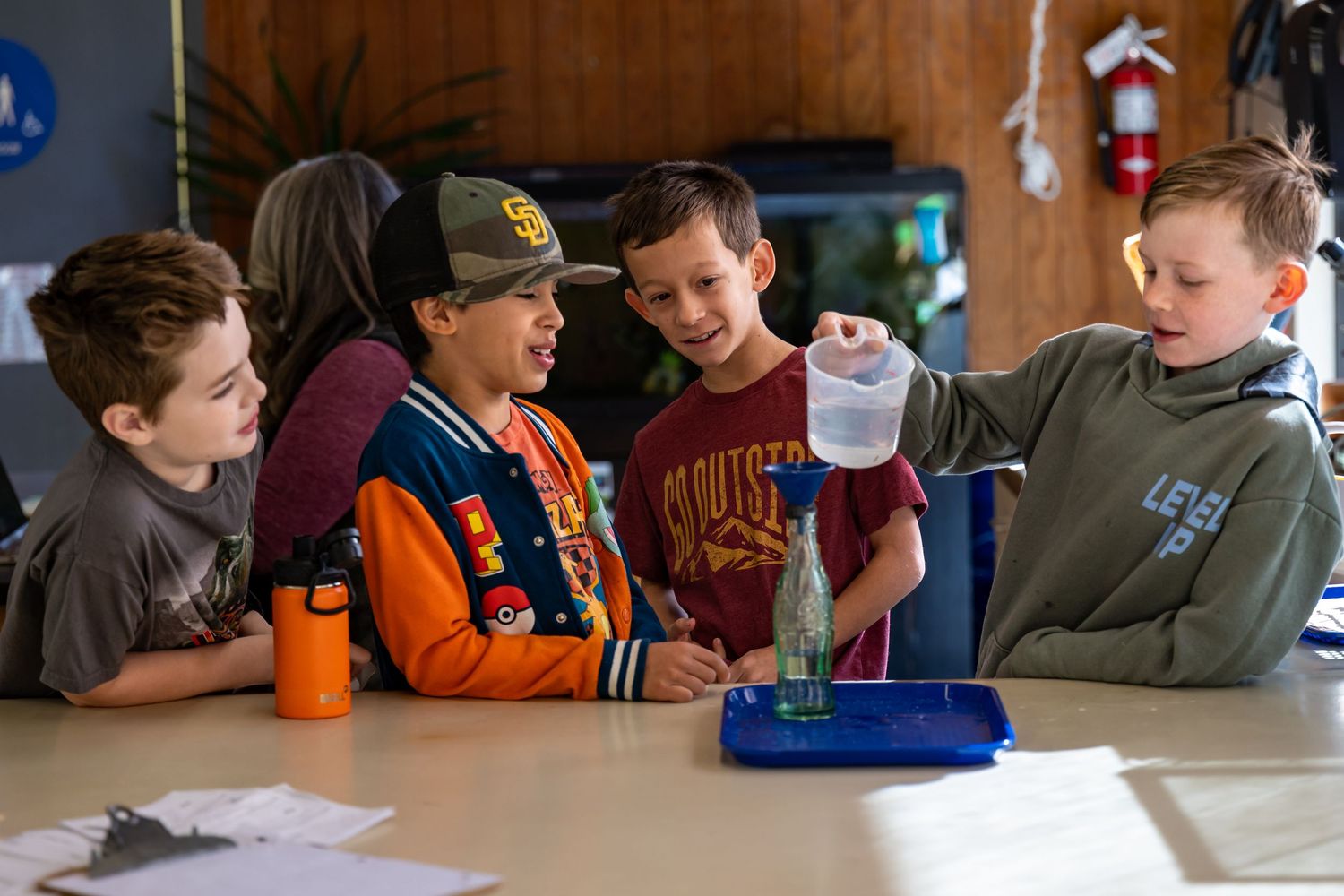 Students sit at tables in a classroom while working together on an educational activity.