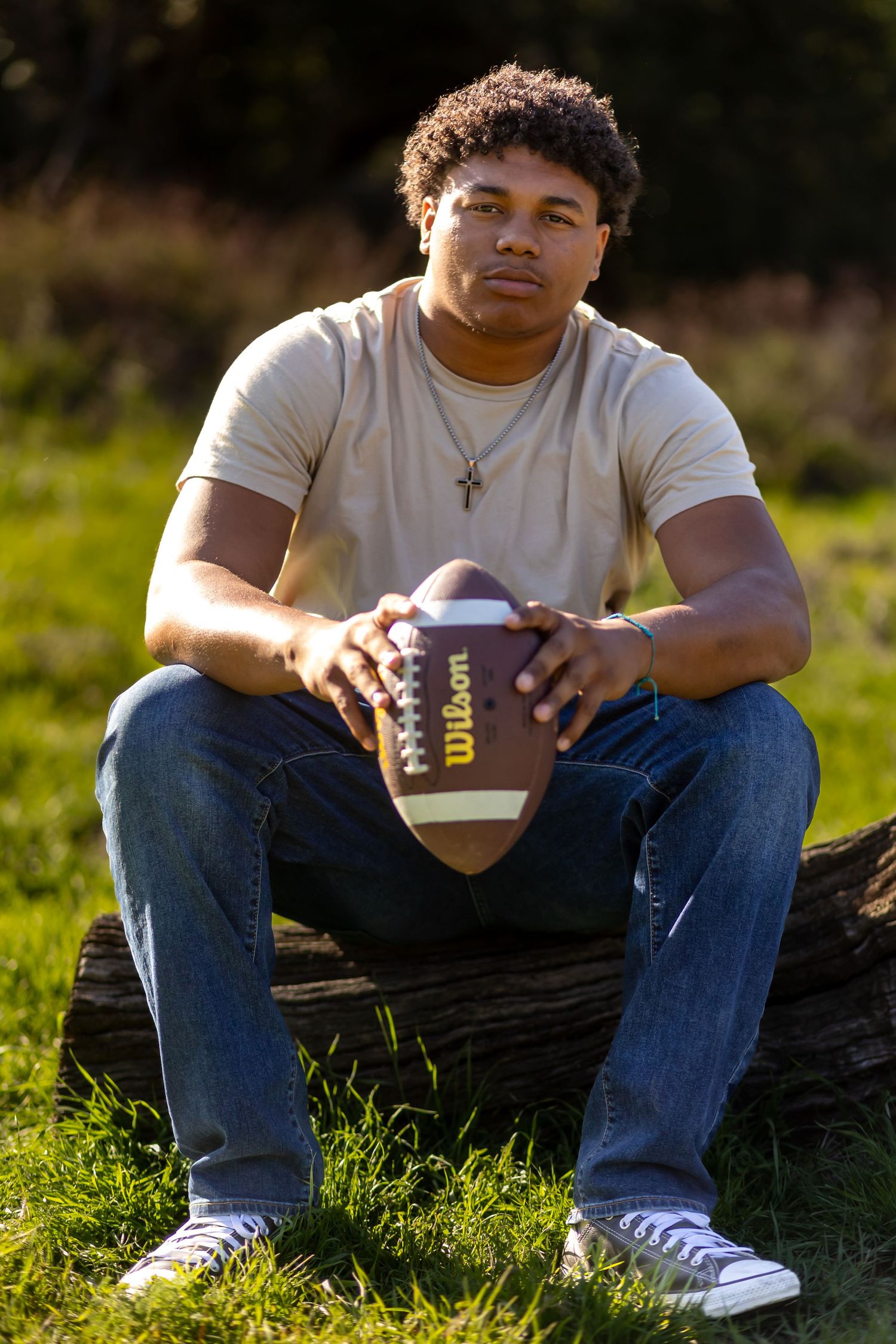 Senior sitting outdoors holding football on fallen log in sunlit field in Yucaipa.
